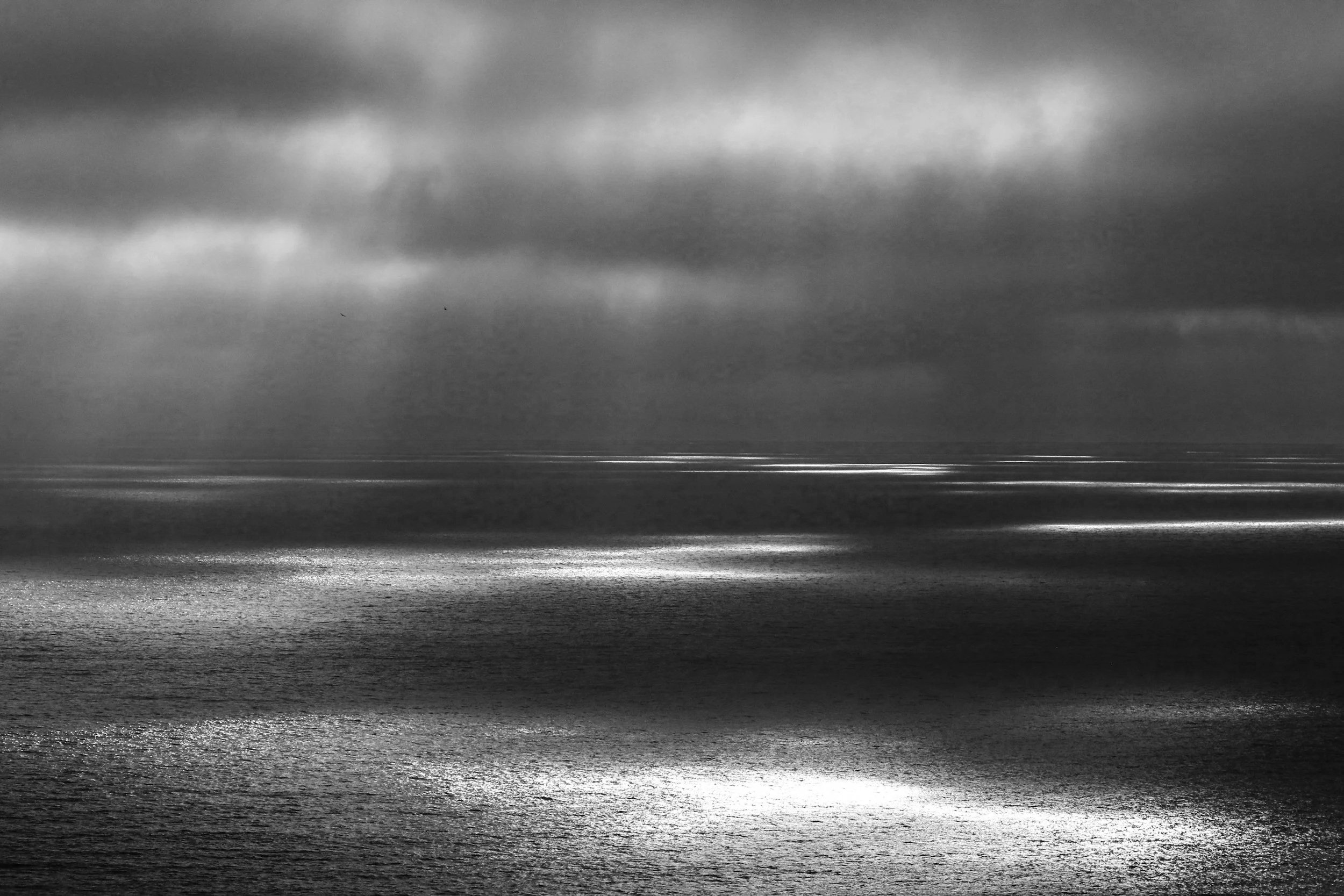 Black and white image of ocean waves with dark, cloudy sky overhead.