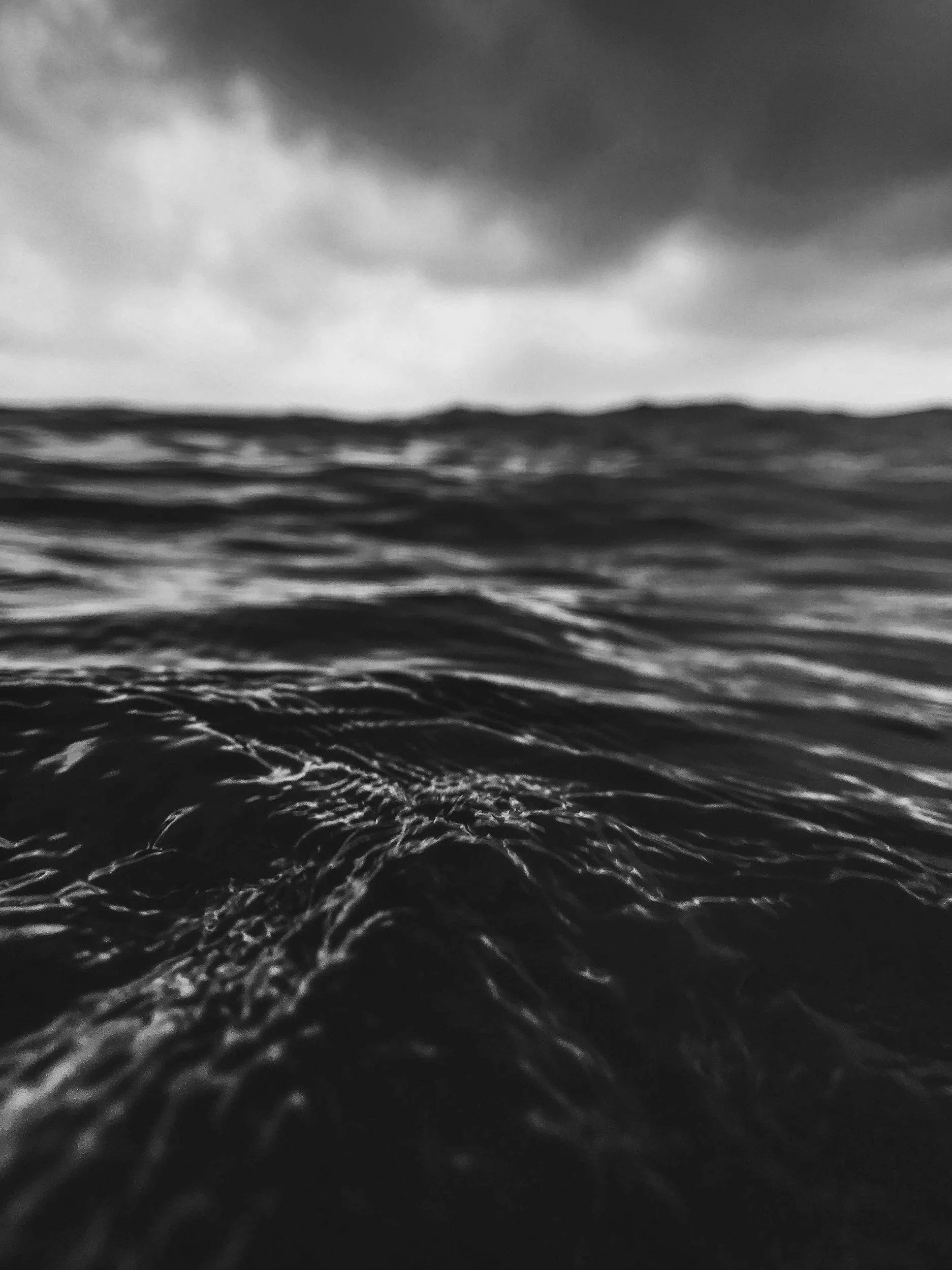 Black and white photo of choppy ocean waves under a cloudy sky.