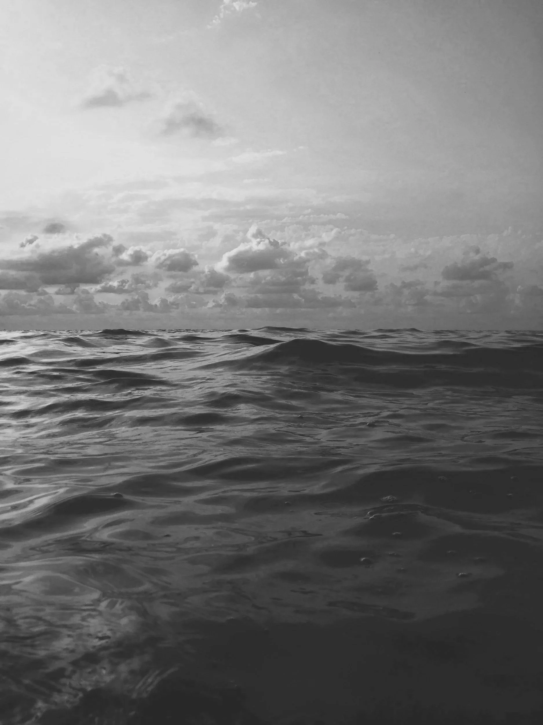 Black and white photograph of the ocean with small waves and a cloudy sky.
