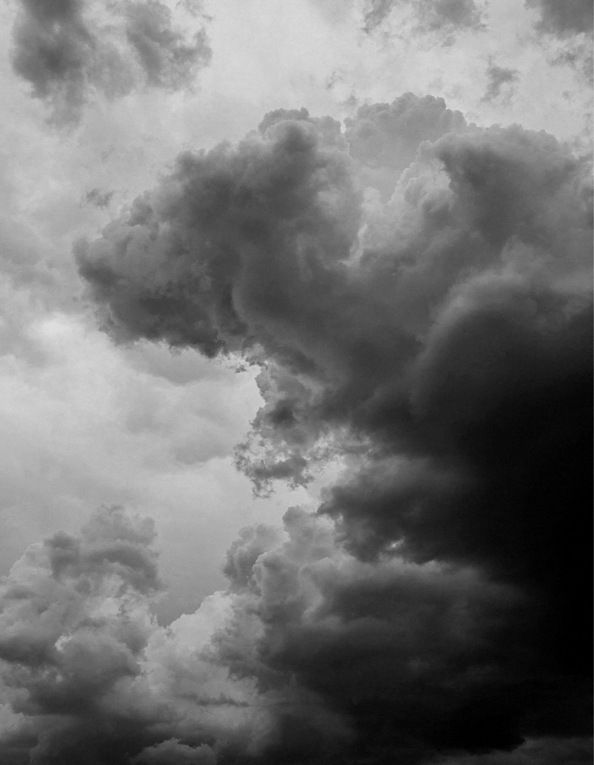 Black and white photograph of dark, dense, and billowing storm clouds in the sky.