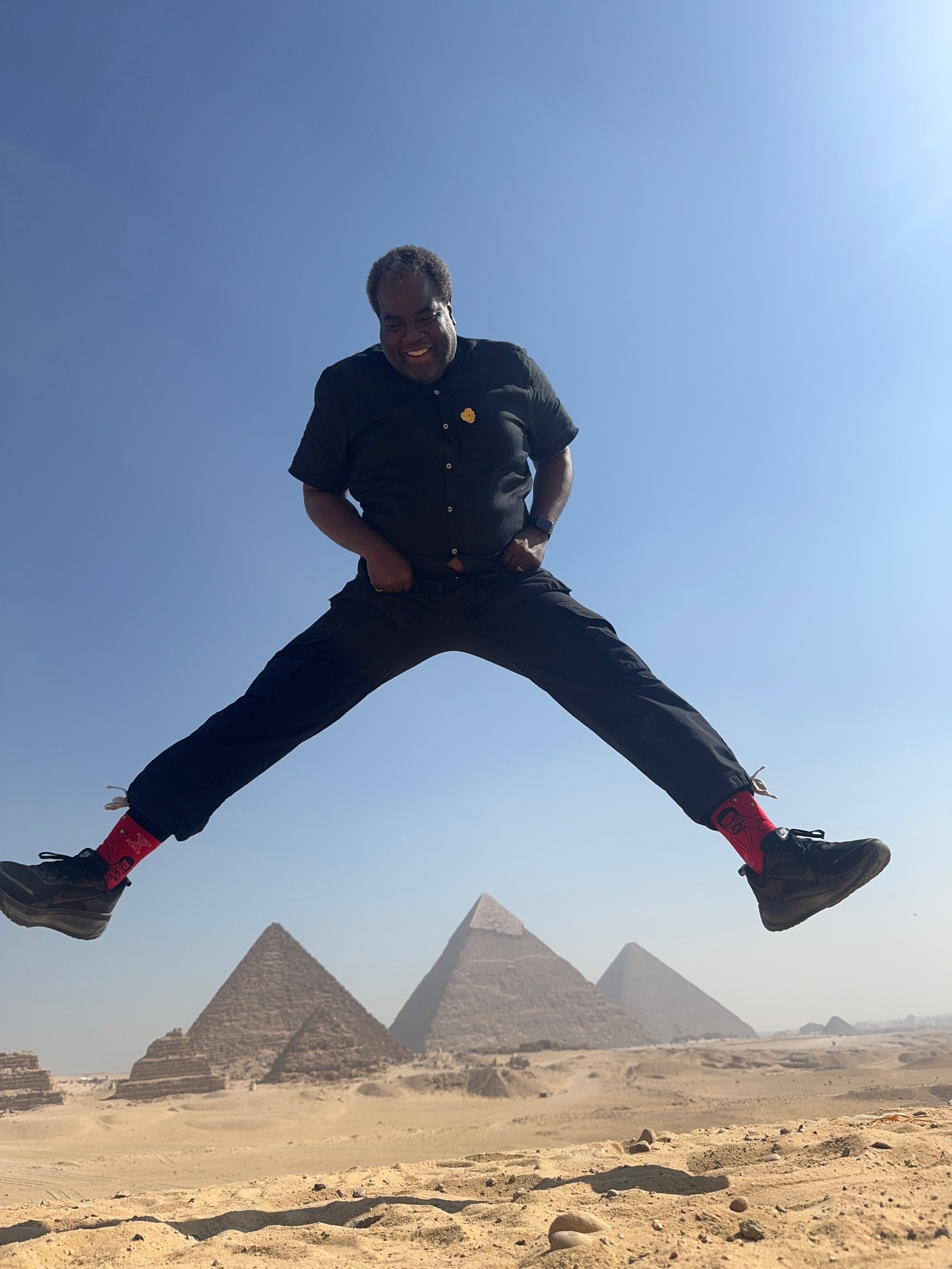 A striking landscape shot of Kenneth Atkins jumping before the Giza pyramids under a brilliant sun, emphasizing the scale, clarity, and cinematic quality of KLA. Media production.