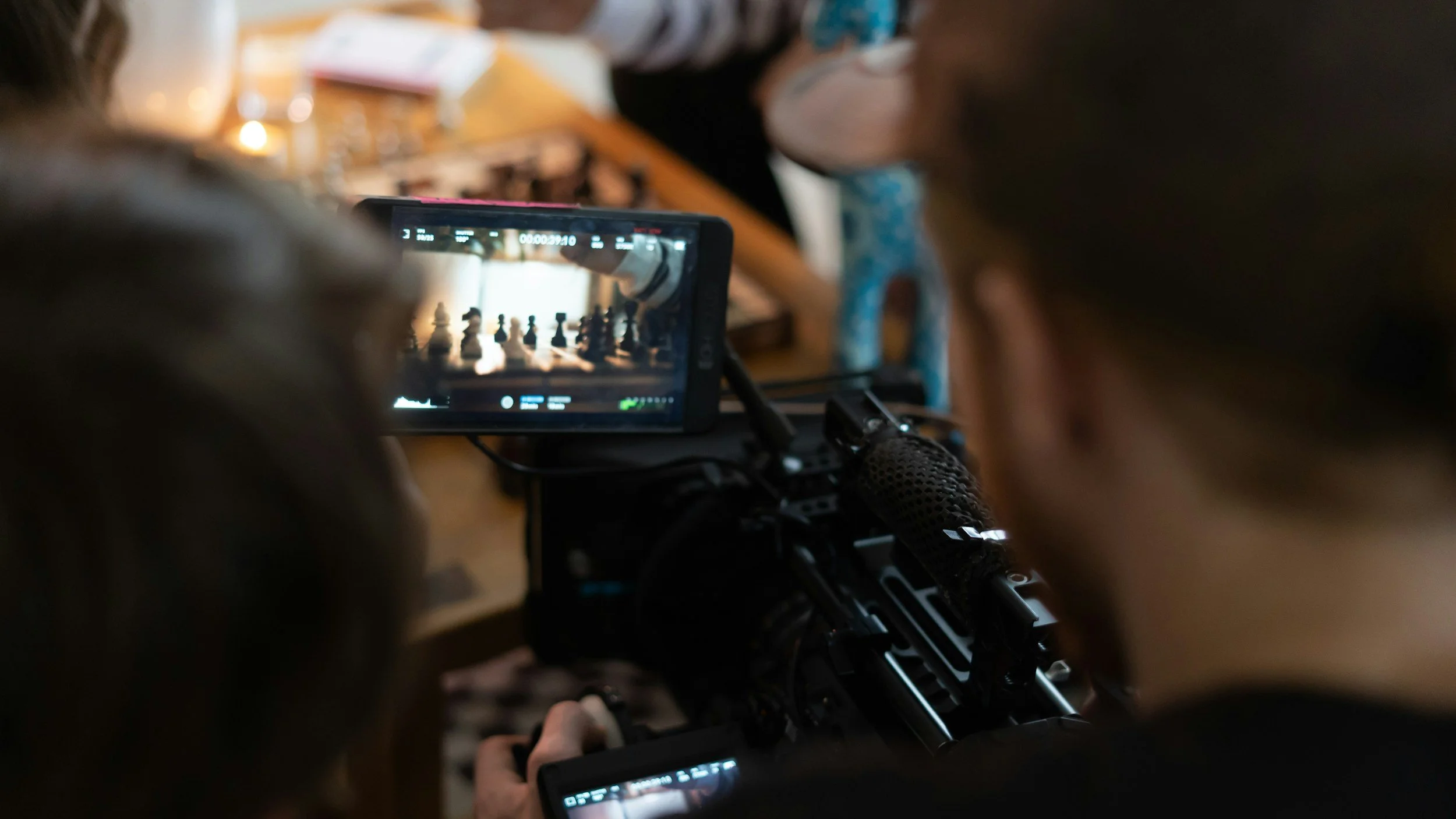 Two people are filming a chess game with smartphones, capturing the chessboard visible on the screens.