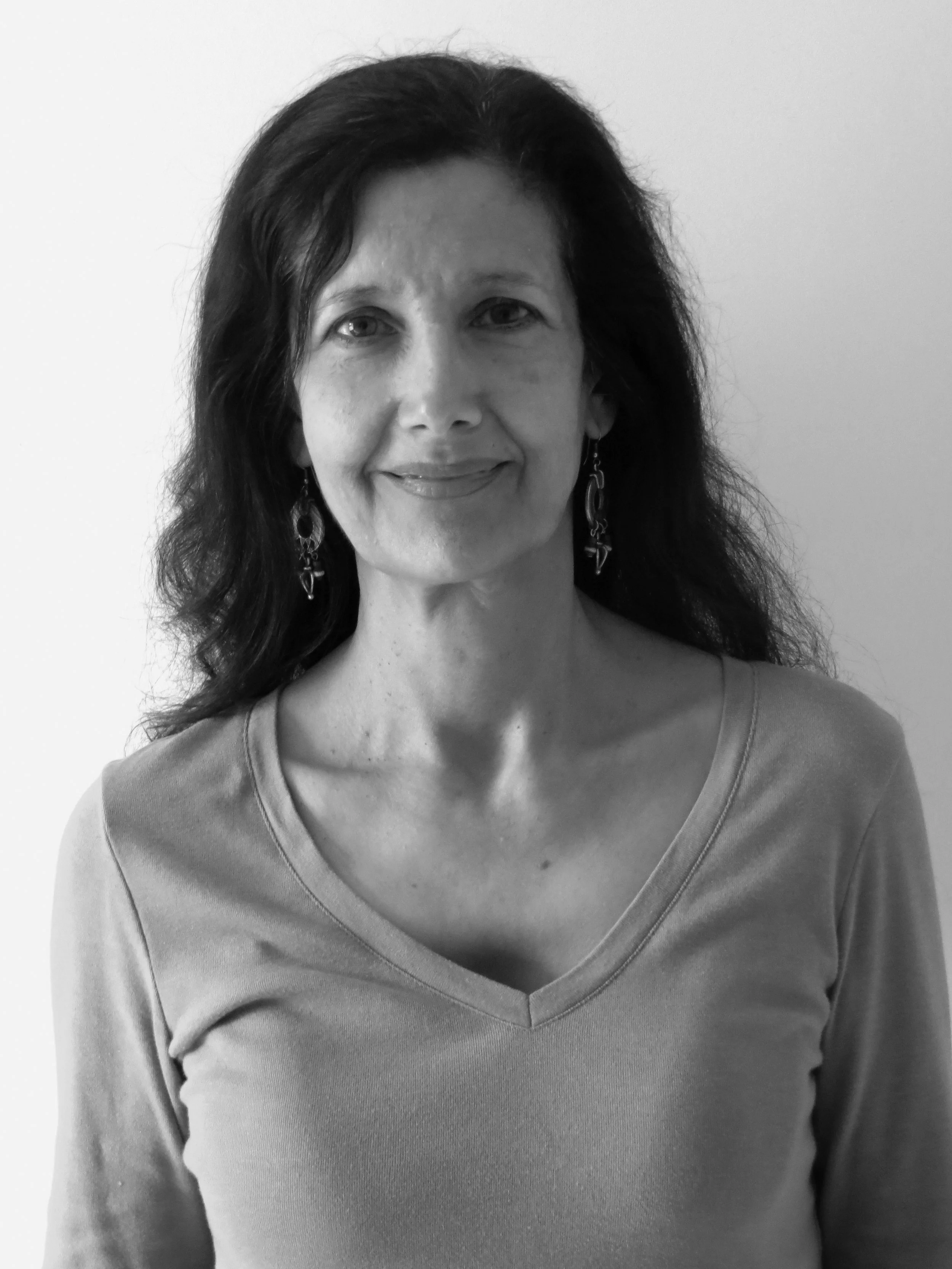 A black and white portrait of a woman with wavy dark hair, earrings, and a V-neck top, smiling softly against a plain background.