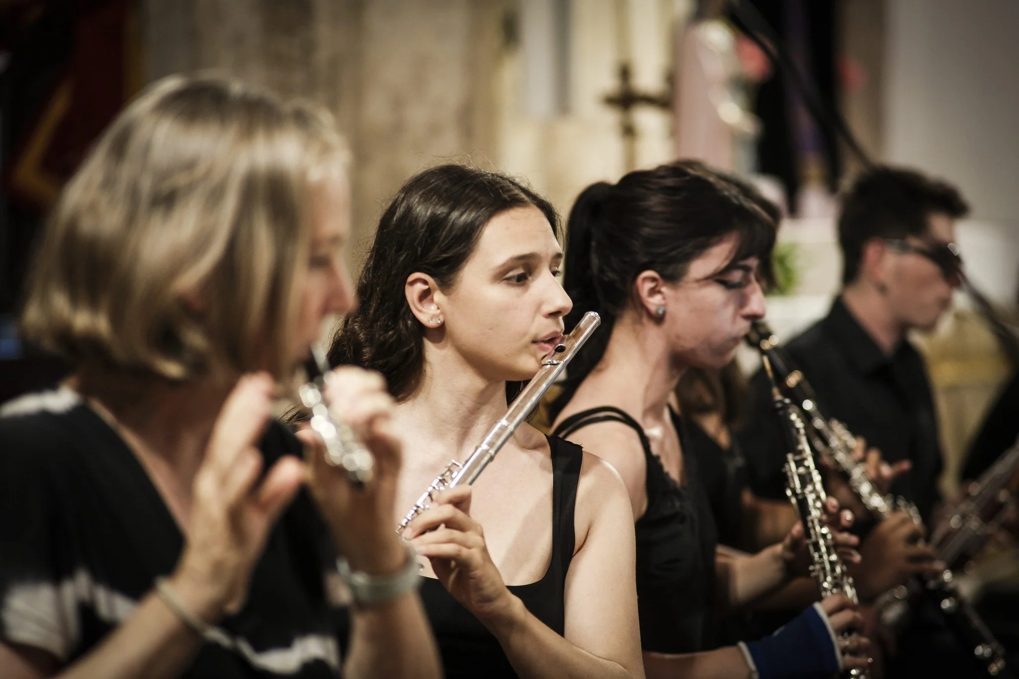 Grupo de músicos tocando flauta e clarinete em uma apresentação, com foco na mulher no centro.