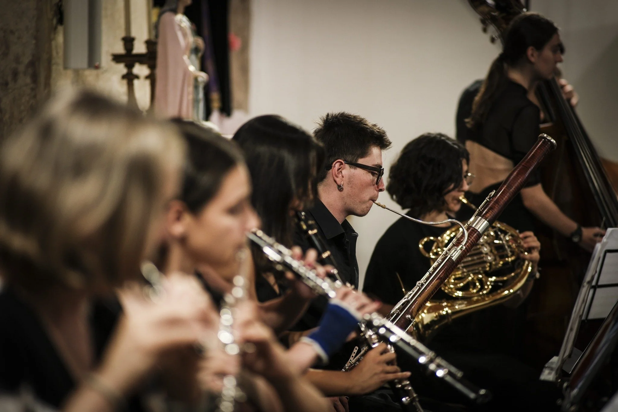 Grupo de músicos tocando instrumentos de orquestra, incluindo flauta, clarinete, fagote e violoncelo.