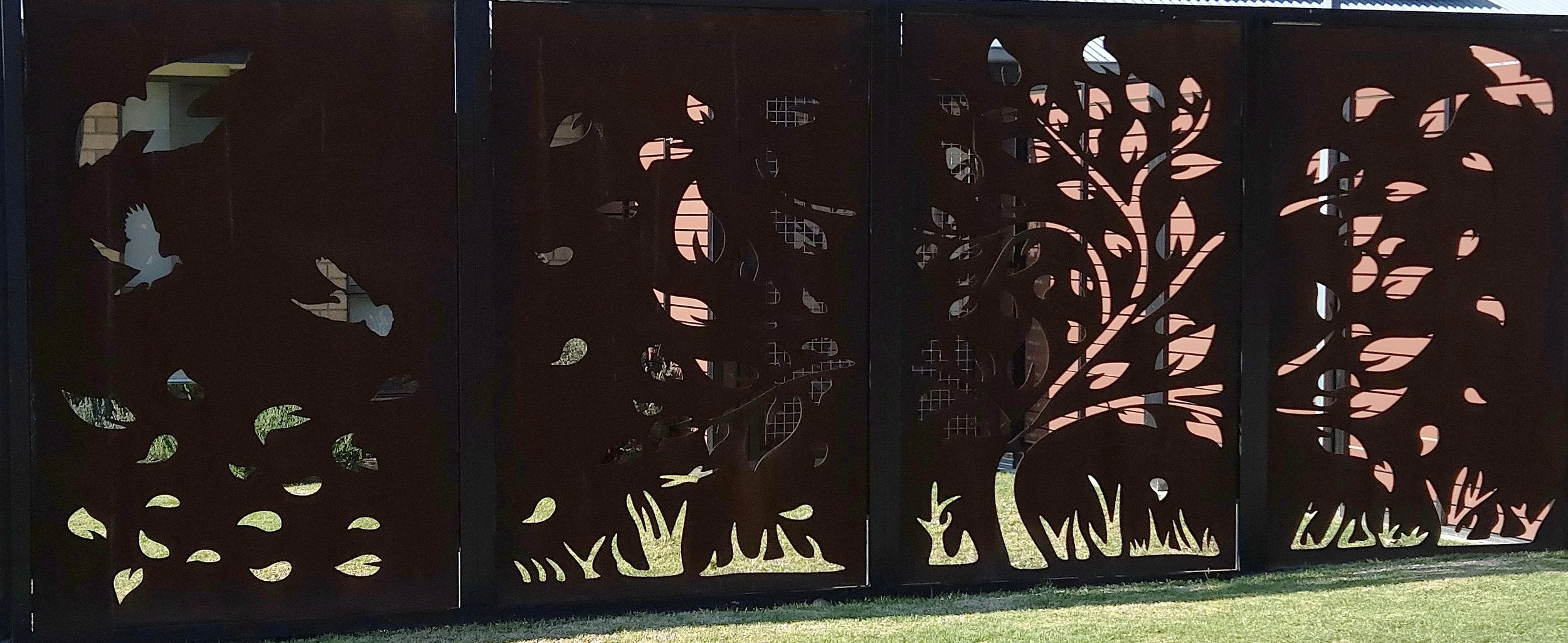 Decorative metal fence with cutout designs of a flying bird, a tree with leaves, and animals like a rabbit, set outdoors.