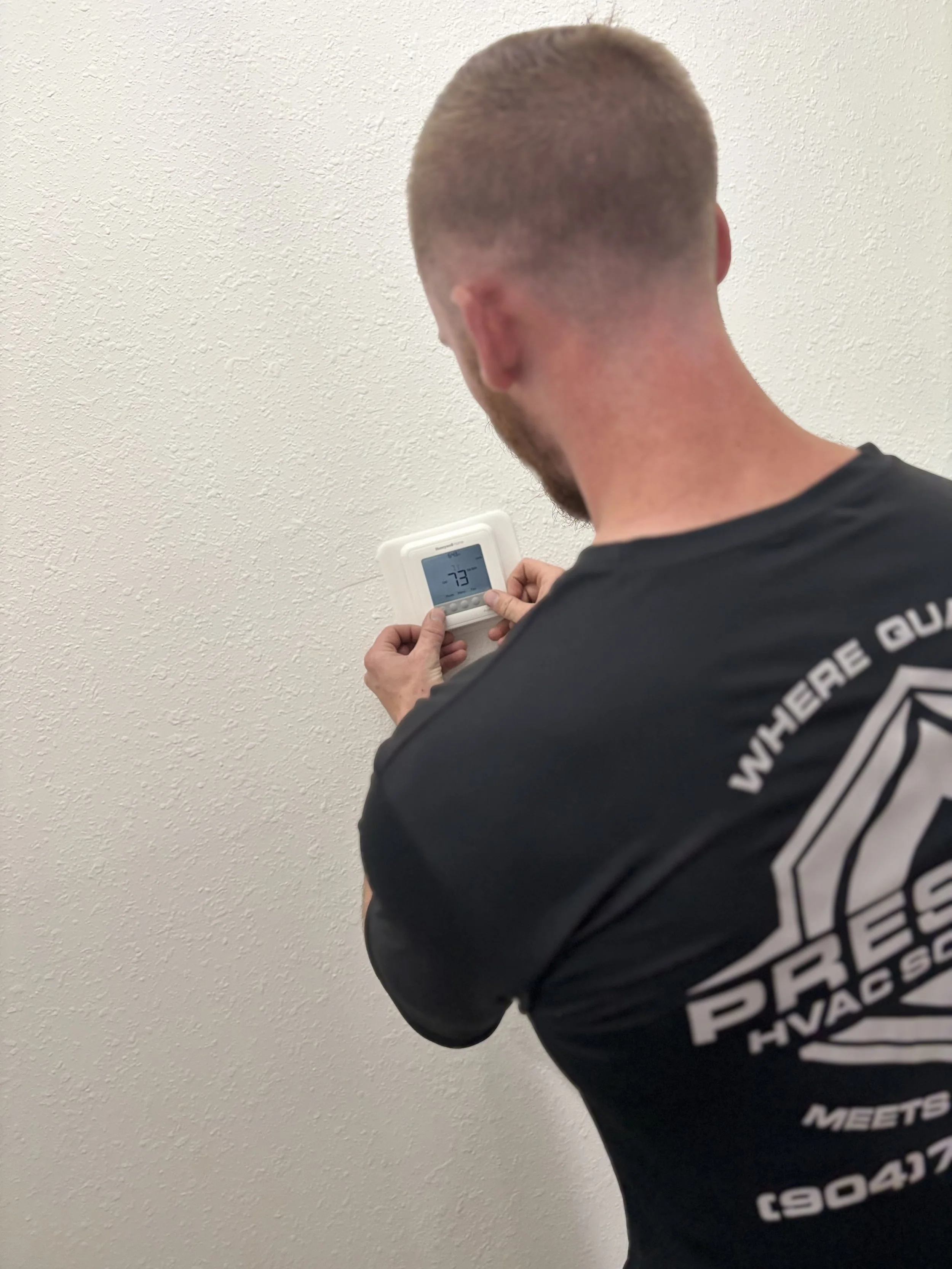 A technician installing or servicing a large, black HVAC duct fan with a blue cover in a room with pink walls.
