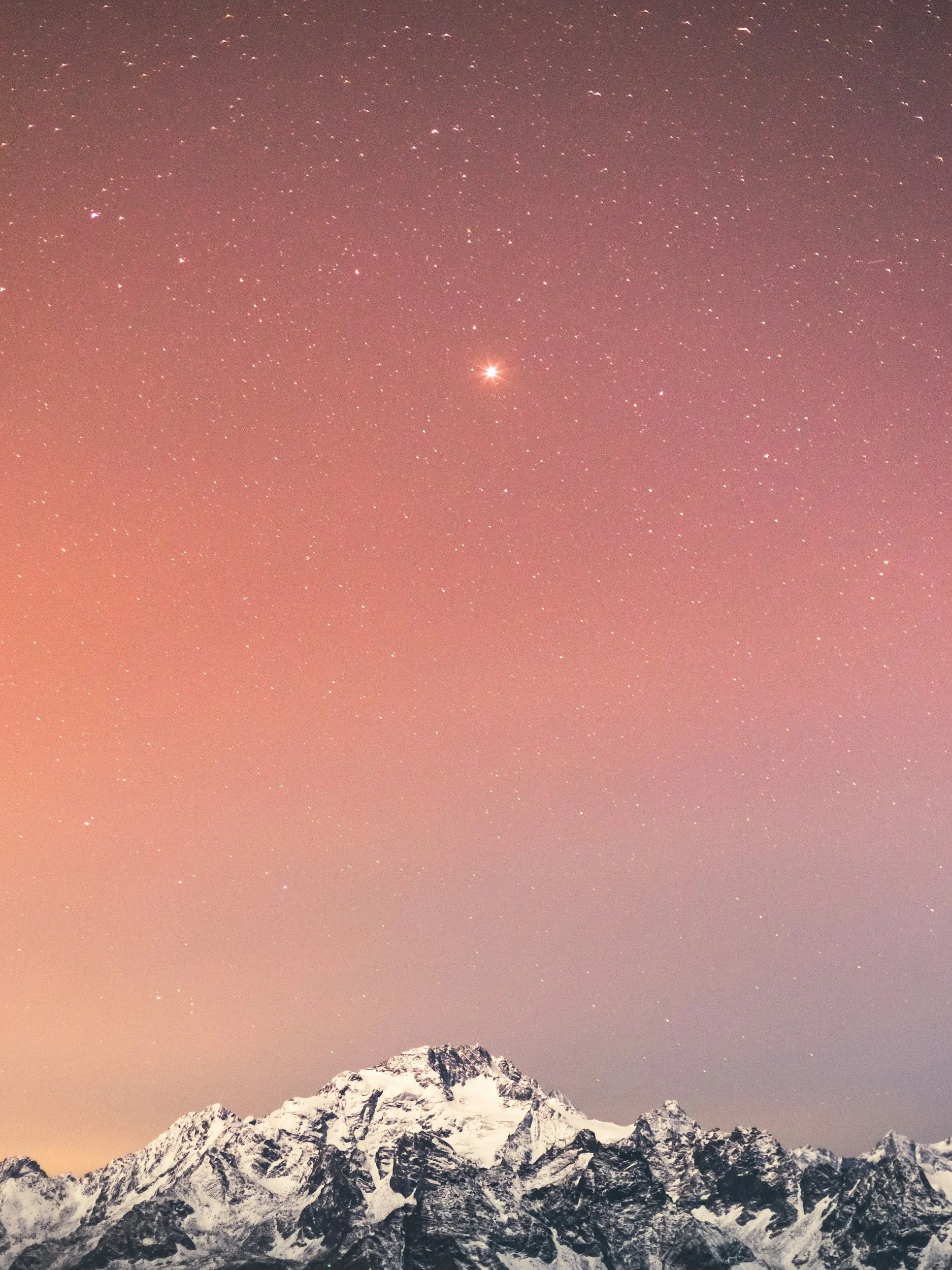 Snow-covered mountain range under a colorful, starry night sky with a bright planet or star visible.