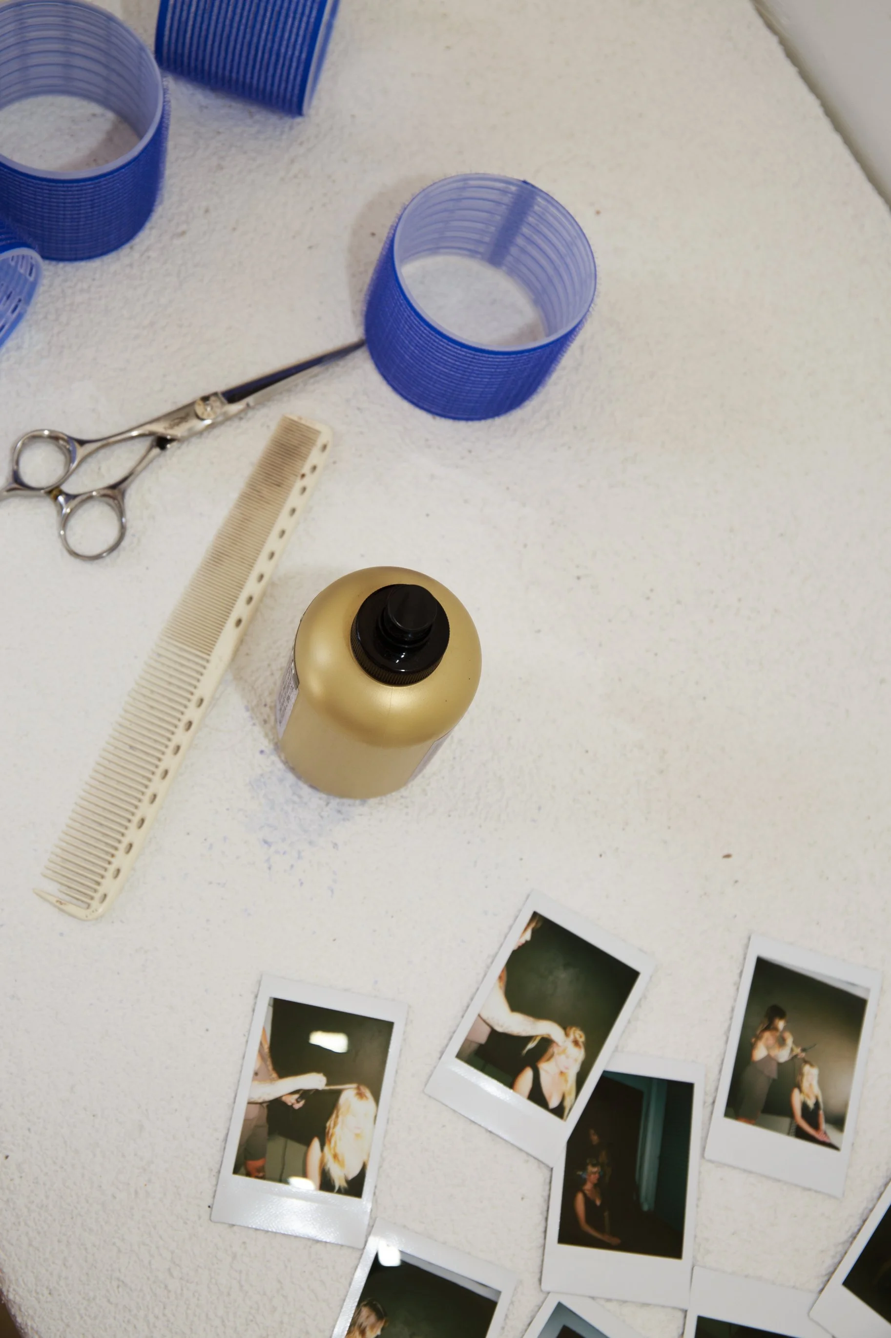 Hairdresser's table with scissors, comb, hairspray, and polaroid photos.
