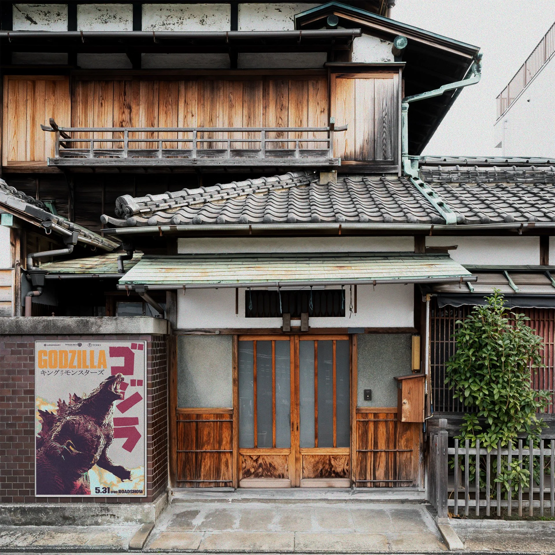 Traditional Japanese building with a wooden entrance, tiled roof, and a green bush on the right. A Godzilla movie poster is on the left wall.