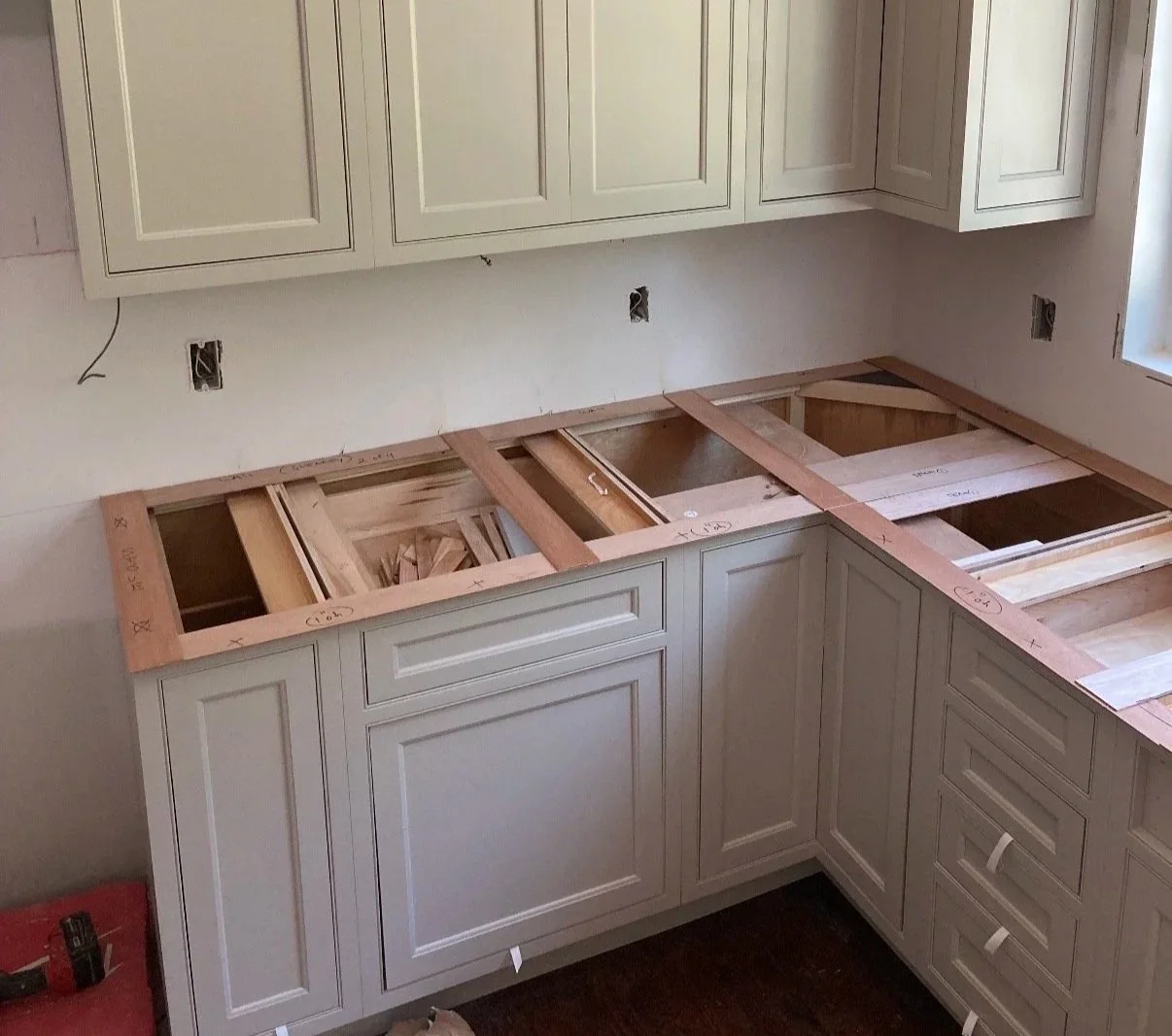 Kitchen cabinets under renovation with countertop removed, exposing the wooden frame and drawers, and electrical outlets on the wall.