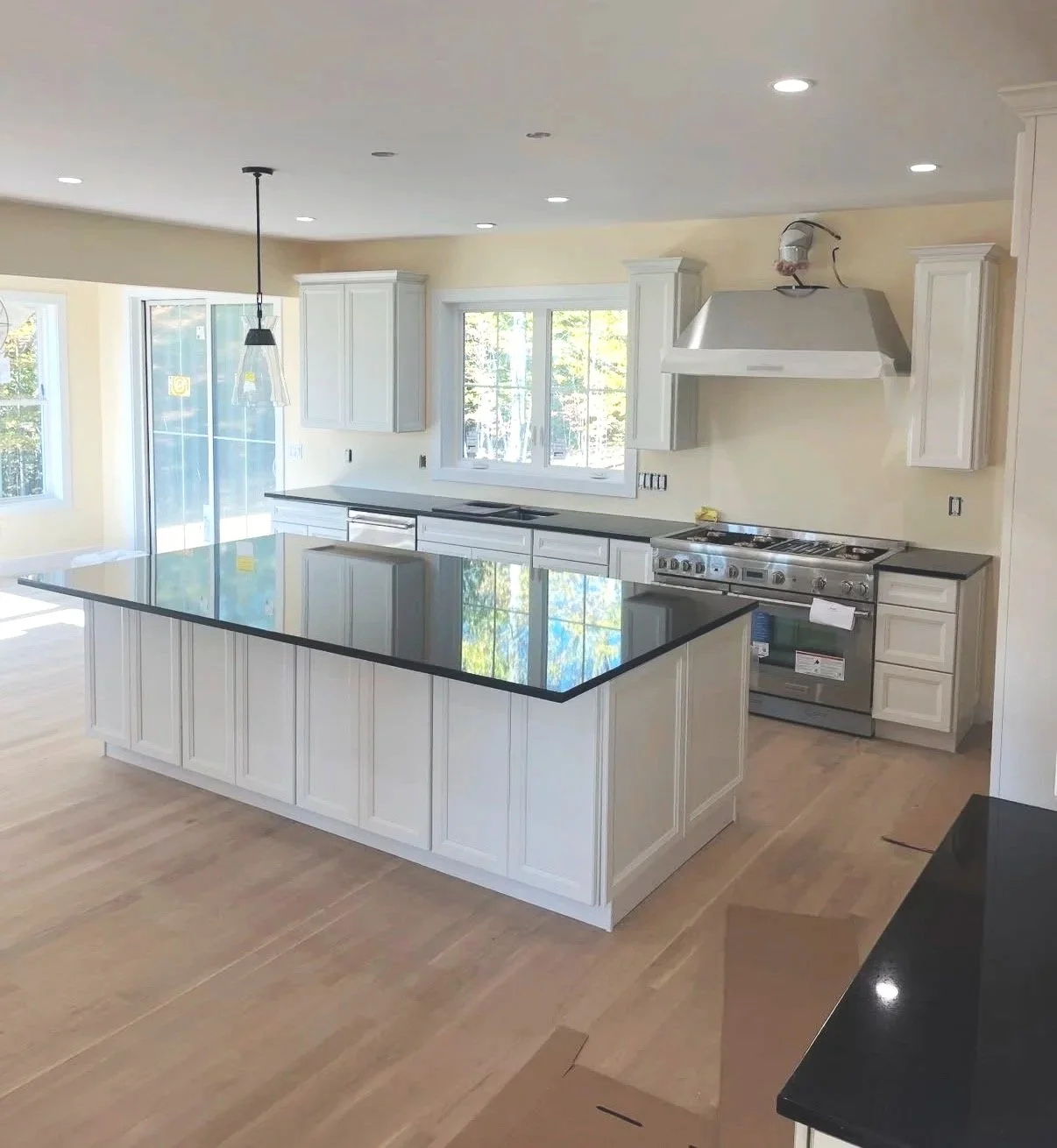 Newly installed modern kitchen with white cabinetry, black countertop island, stainless steel range, and large window with a view of trees outside.