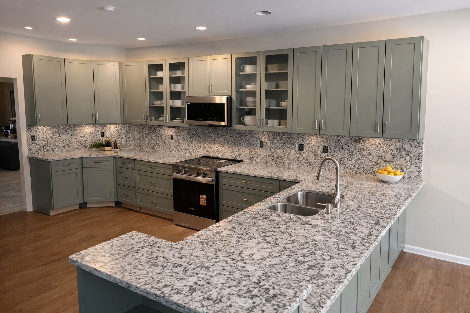 Kitchen with green cabinets, granite countertops, and stainless steel appliances, including an oven and microwave. There is a bowl of lemons on the counter near the sink.