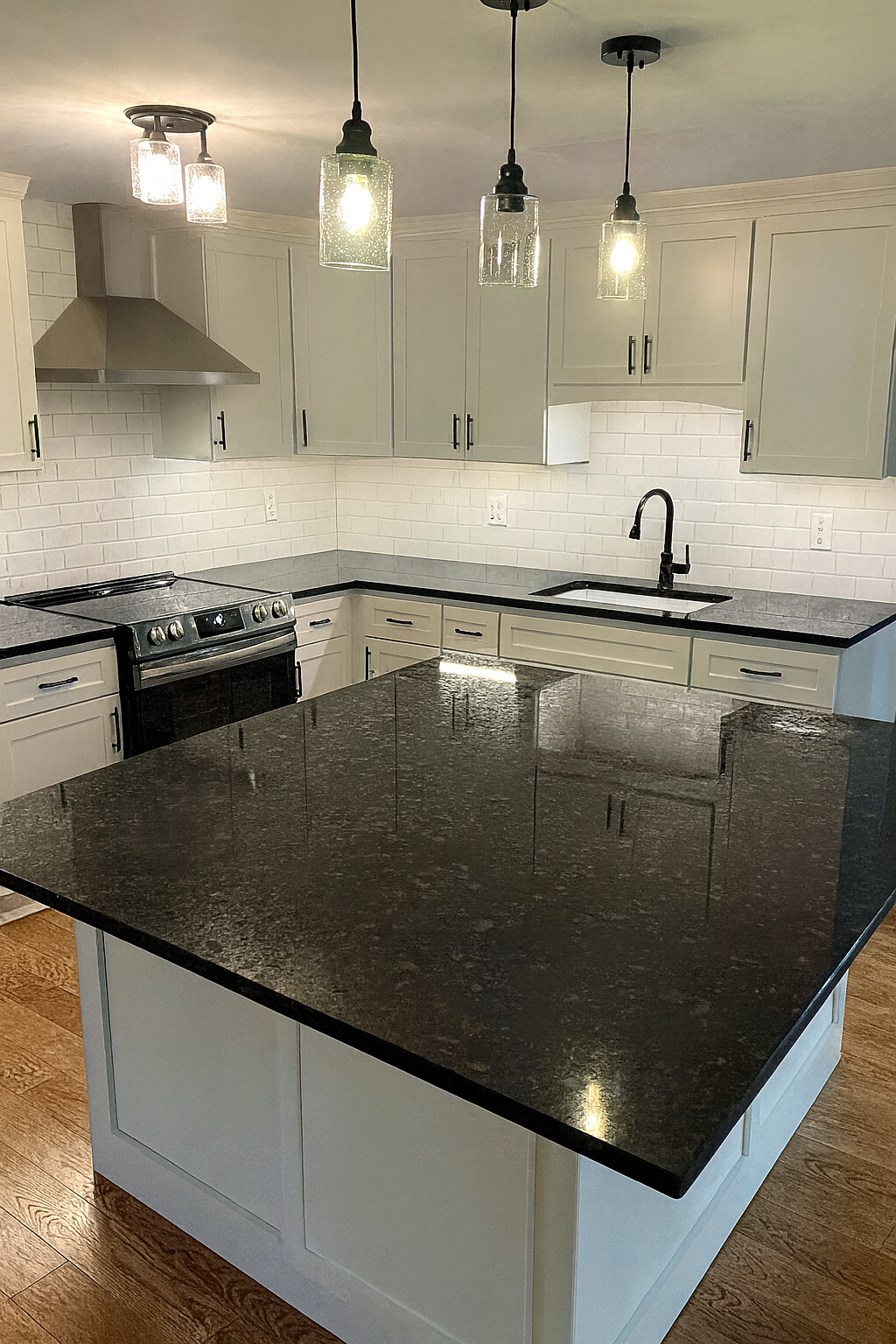 Modern kitchen with white cabinets, black countertops, stainless steel stove, and black faucet, with pendant lights hanging above an island.