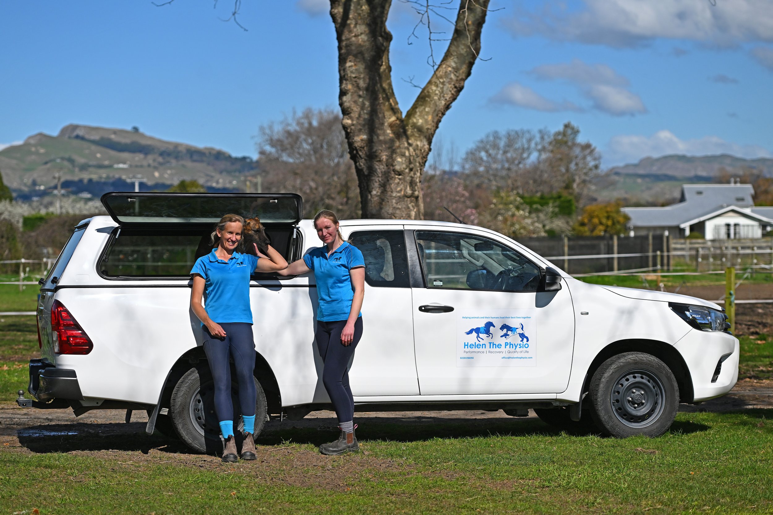 Helen the Physio team - Helen, Molly & Rhubarb the dog, beside white Utility vehicle