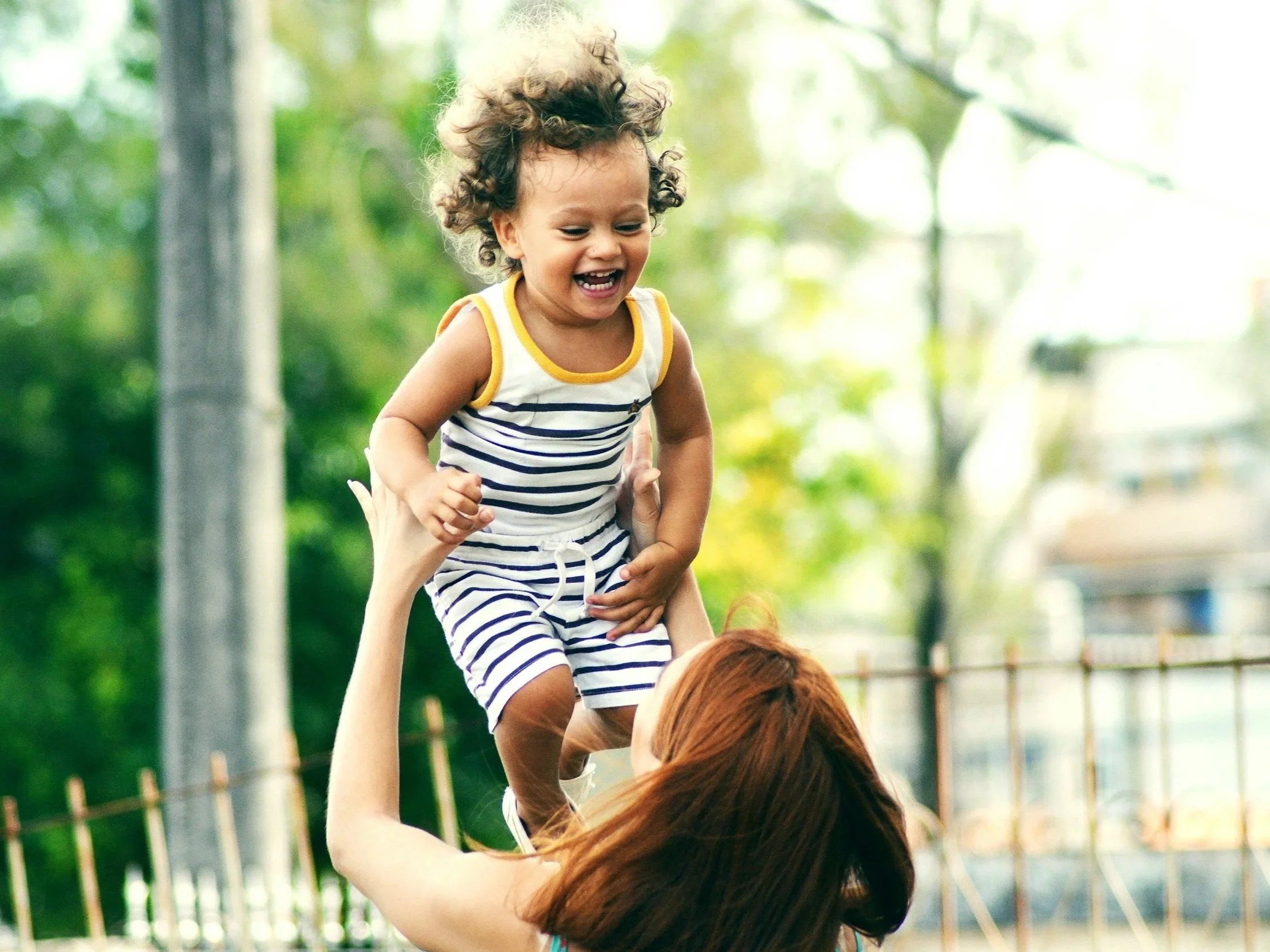 Adult lifting joyful toddler in the air outdoors.