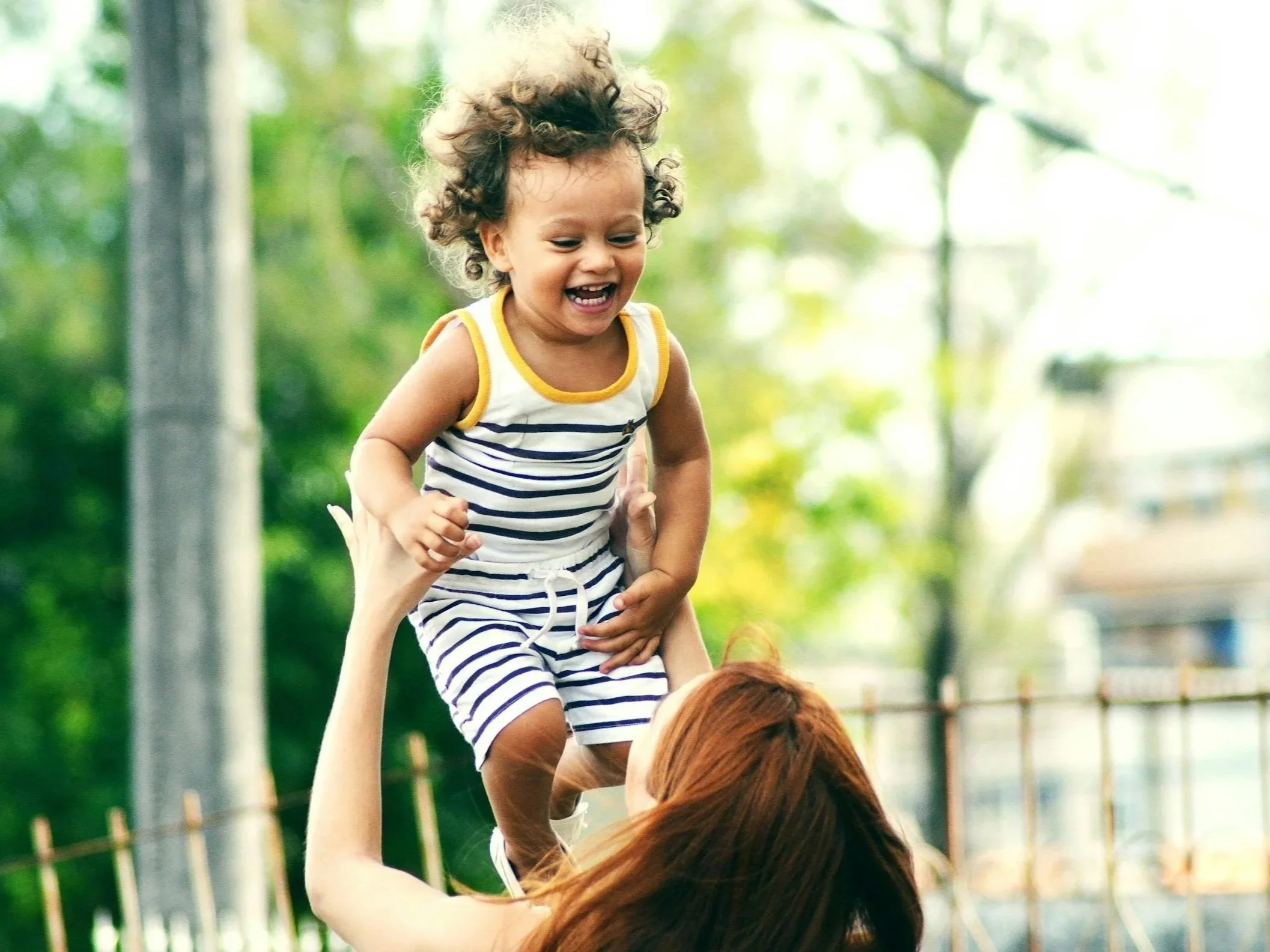 Adult lifting joyful toddler in the air outdoors.