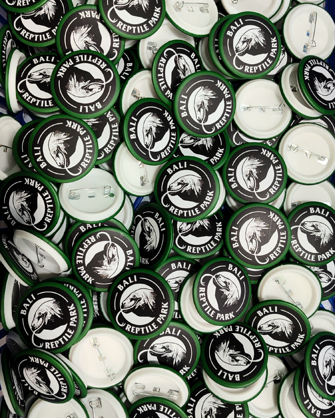 A pile of round buttons with a black and white logo of a dinosaur head and the text 'BALI REPTILE PARK' around the image.