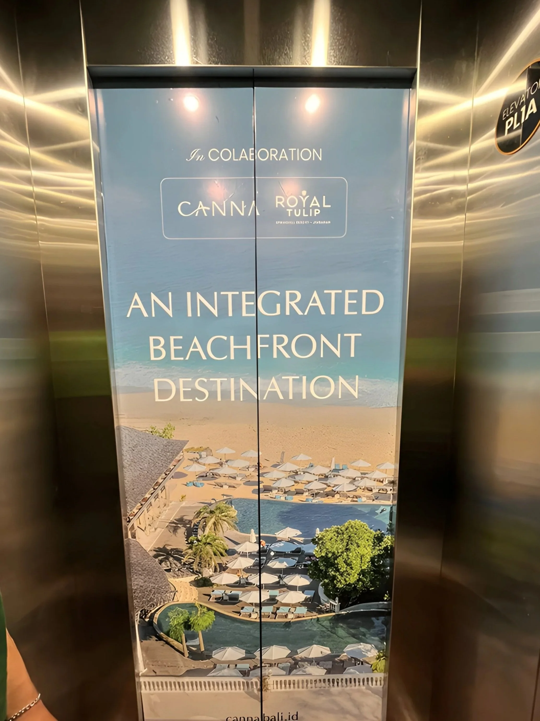 LED elevator door advertising an integrated beachfront destination with a view of a pool, sandy beach, and umbrellas.