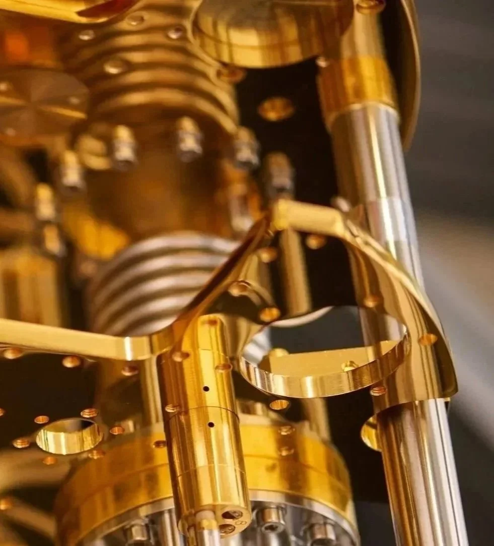 Close-up of a shiny, gold-colored mechanical component with intricate details and multiple small screws and cylindrical parts.