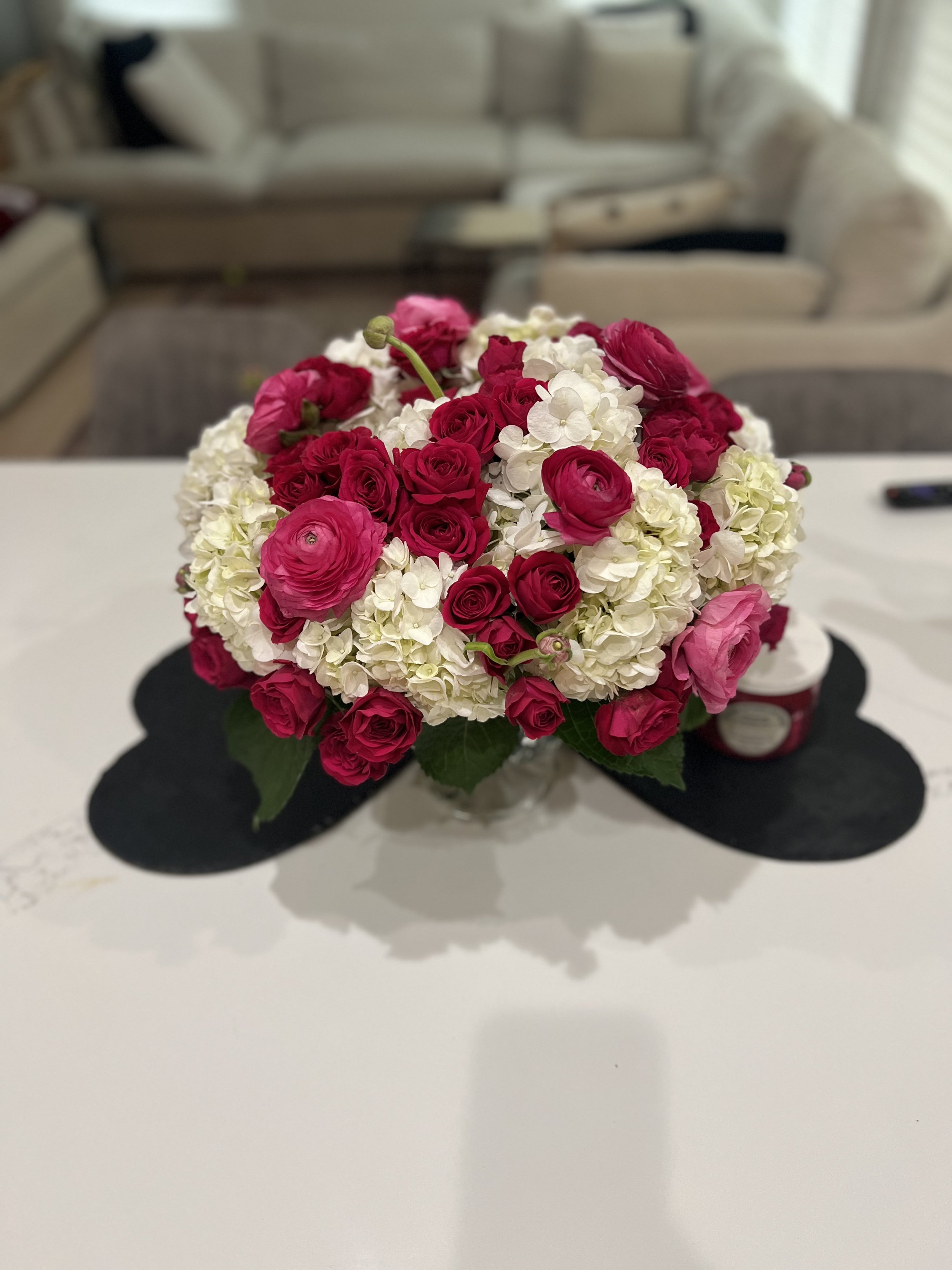 A bouquet of pink and white flowers on a white table in a room with a beige sofa and armchair in the background.