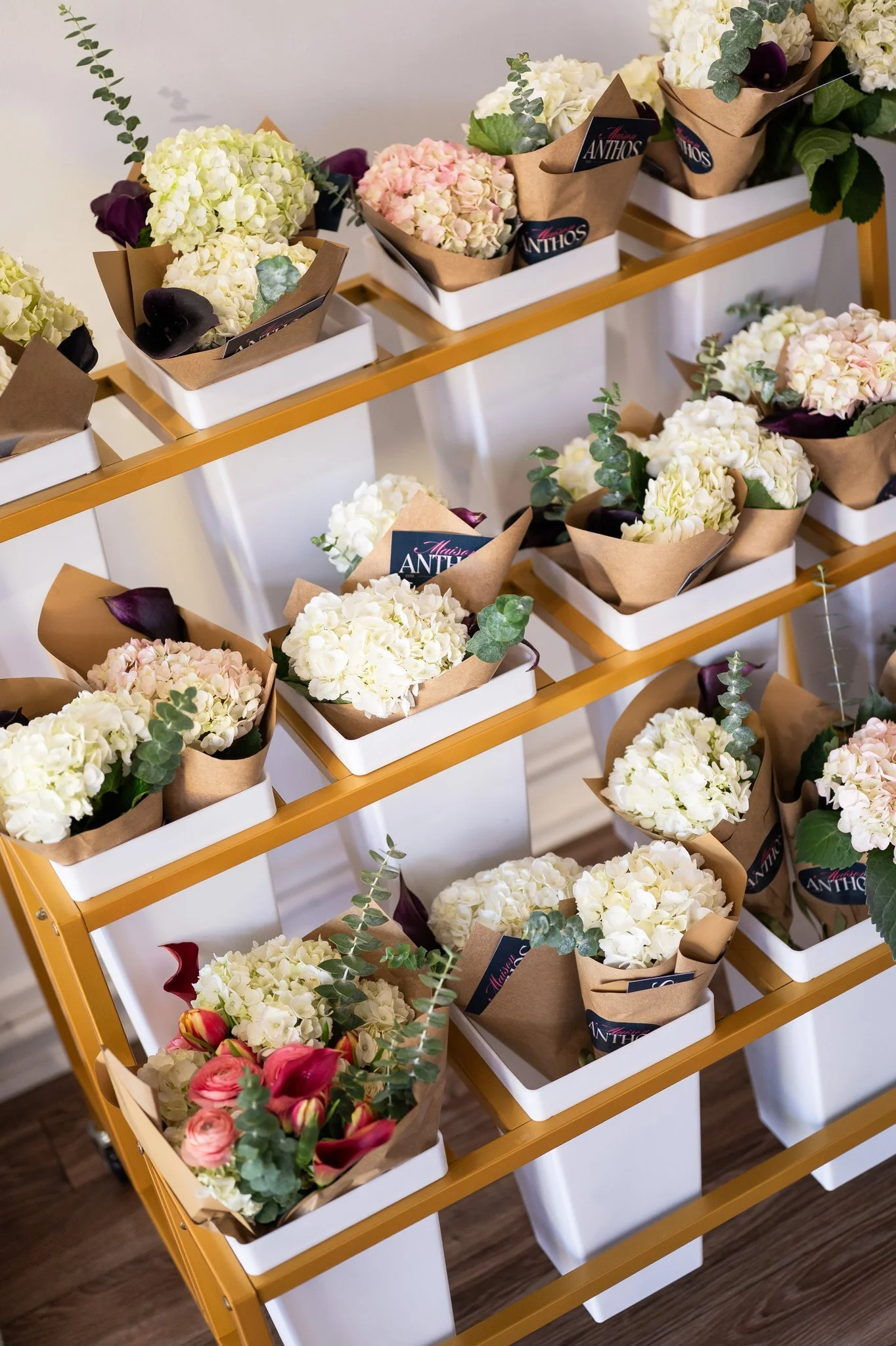 Multiple bouquets of white, pink, and purple flowers wrapped in brown paper and displayed in white holders on a yellow metal cart.