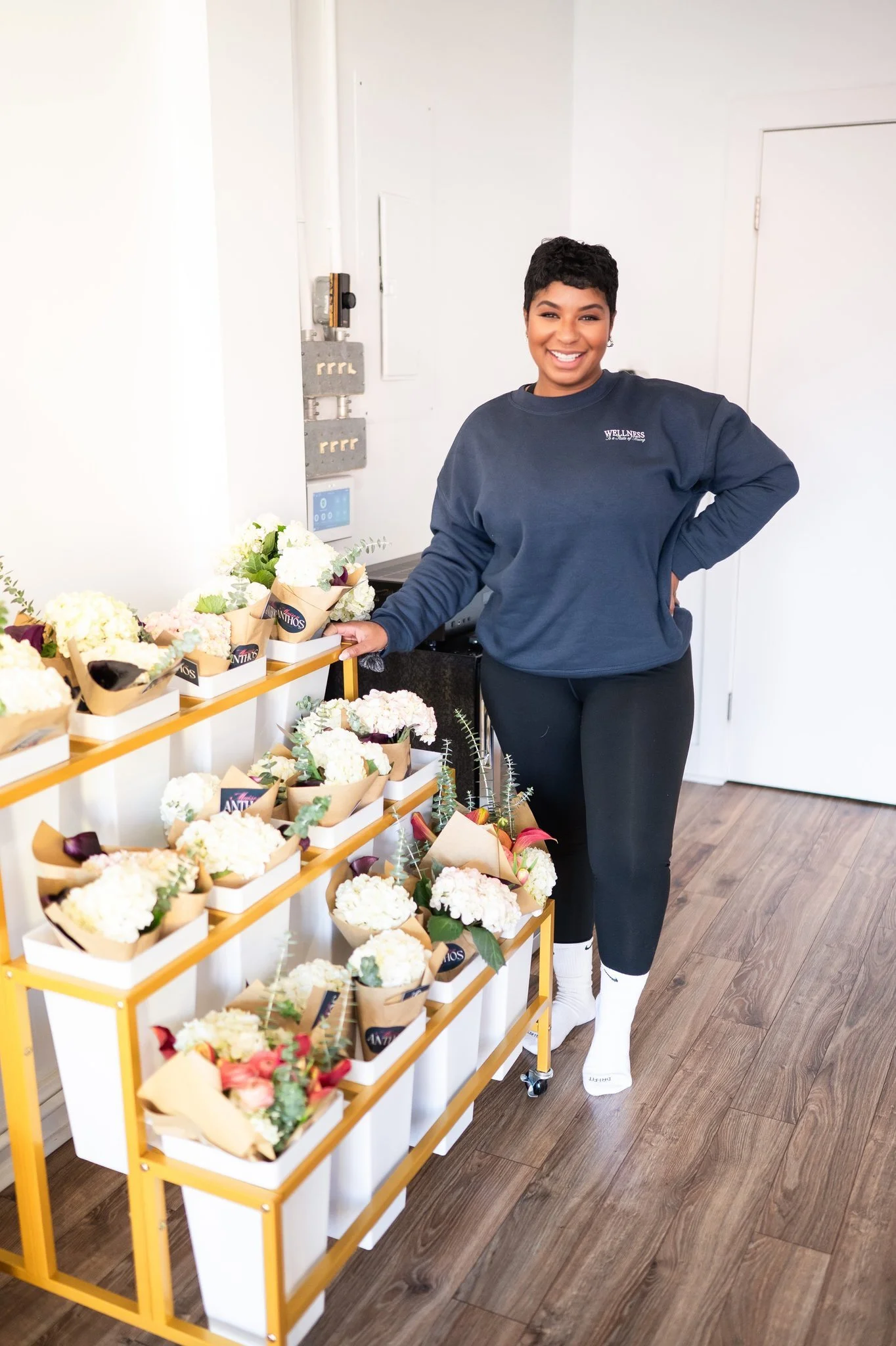 A smiling woman standing next to a yellow cart with an array of flower arrangements in bouquets.