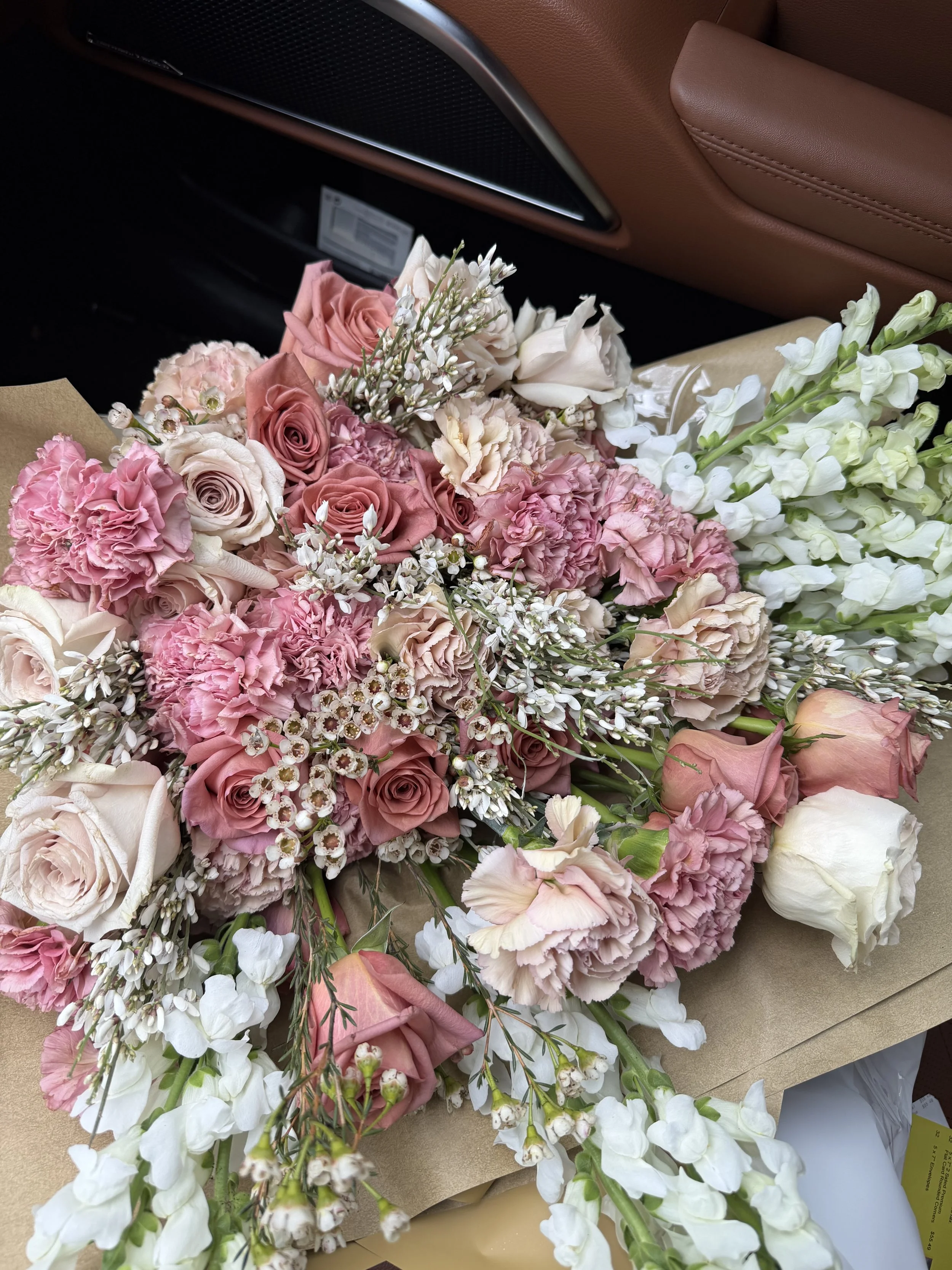 A large bouquet of pink and white roses, carnations, and other flowers placed on a beige paper wrapping inside a car.