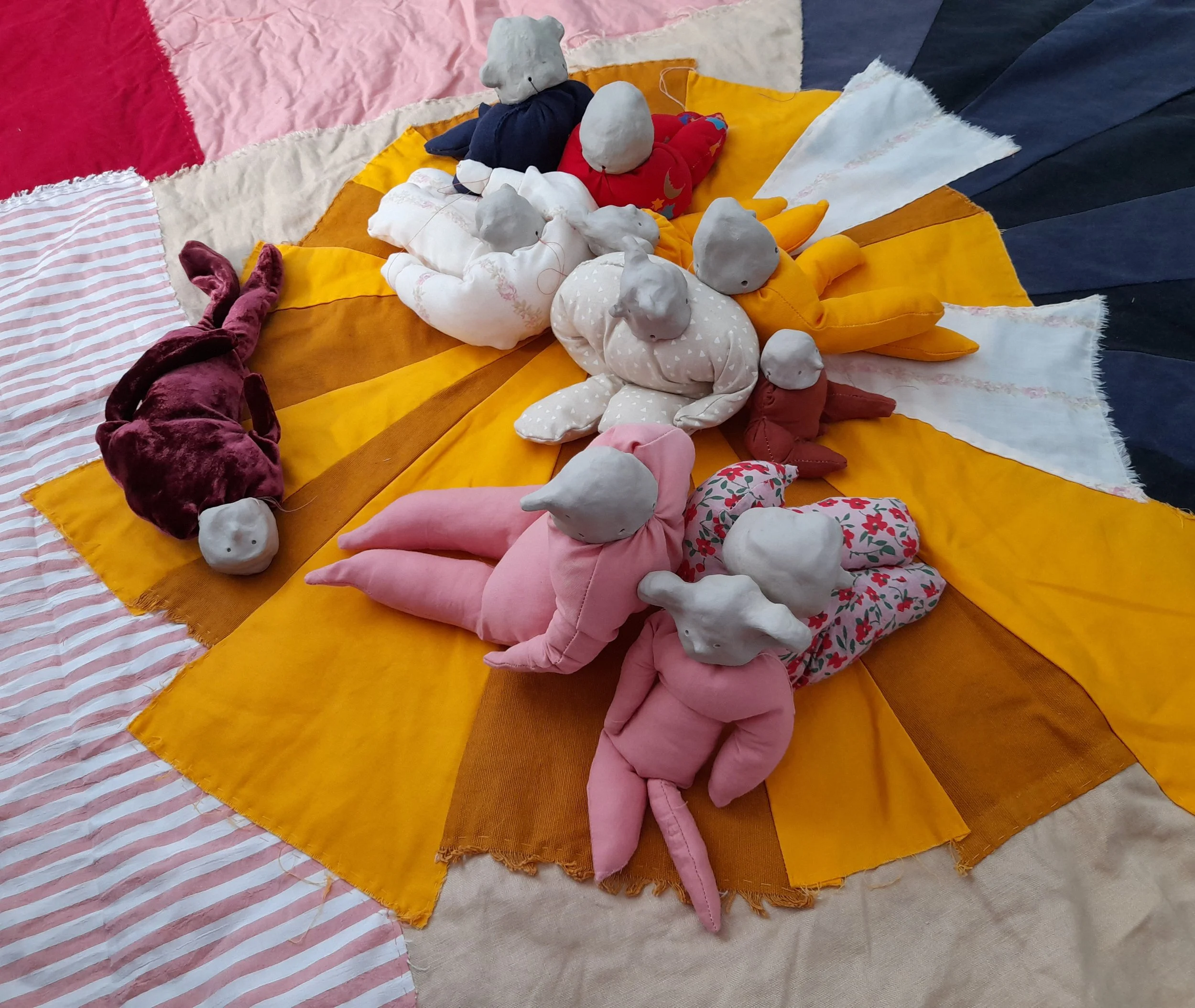 A colorful arrangement of handmade cloth and plush mouse puppets arranged on a multicolored fabric background.