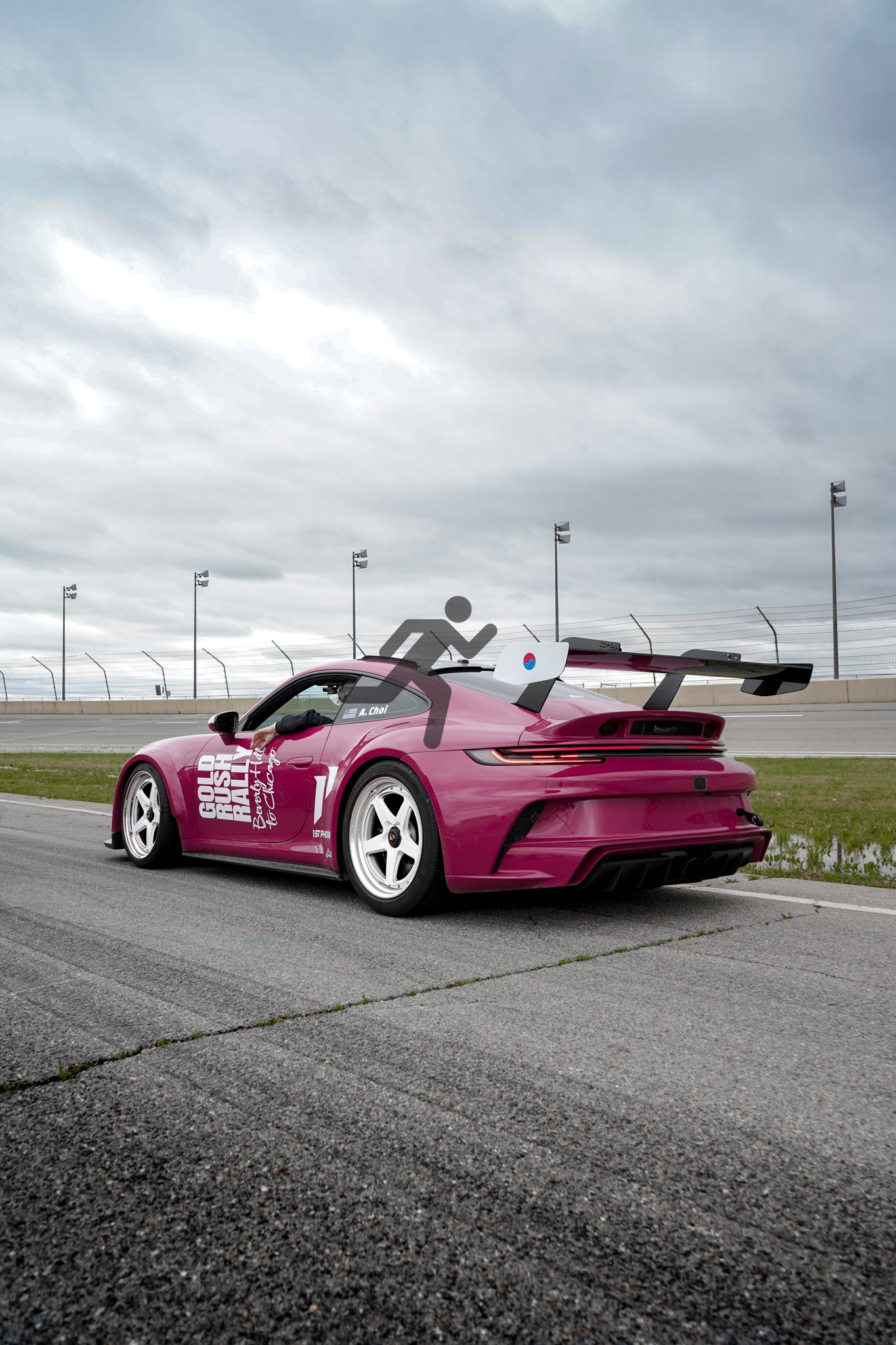 A pink race car on a racetrack with a large rear wing and white wheels, under a cloudy sky.