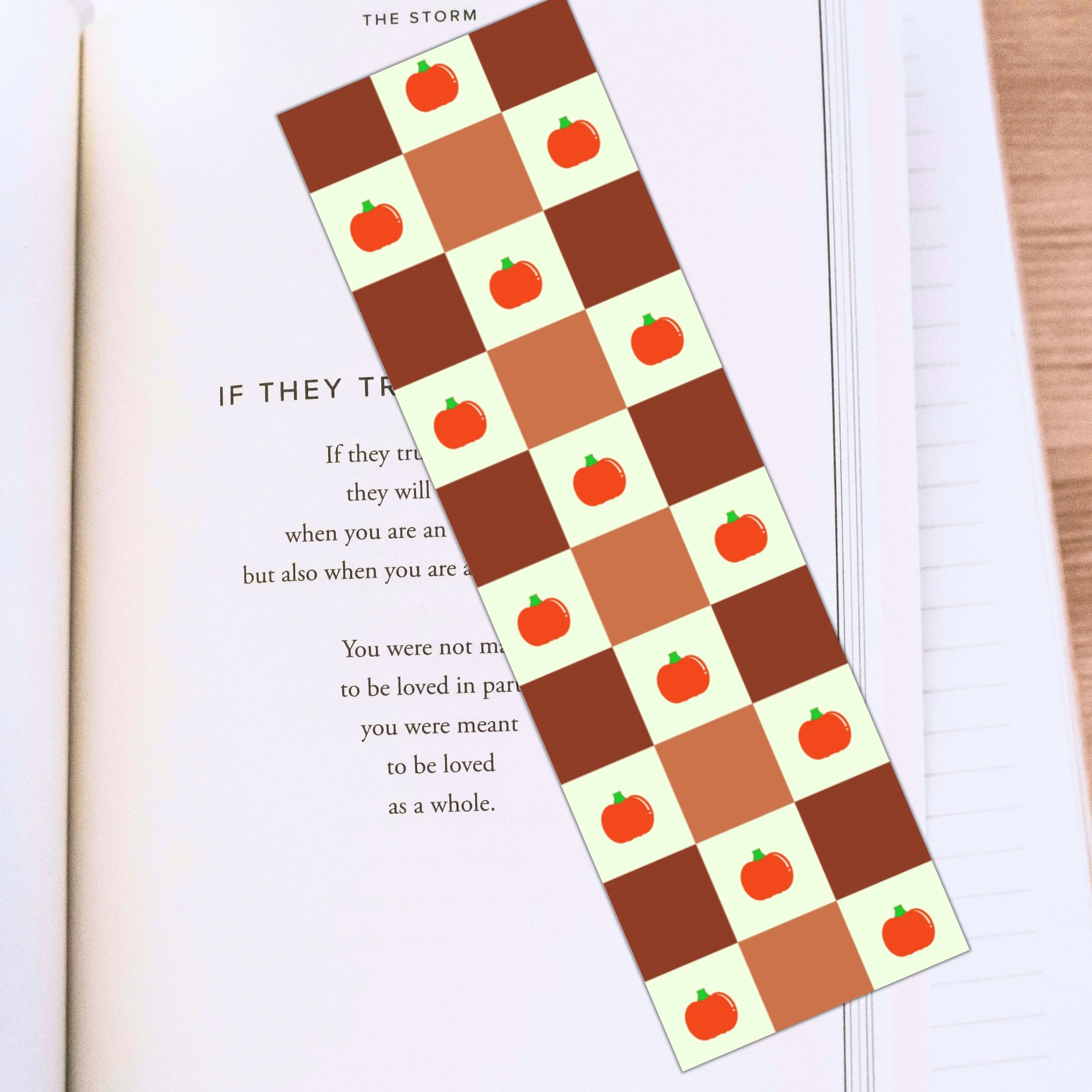 A bookmark with a checkered pattern of pumpkins in green and orange shades, placed over an open book.