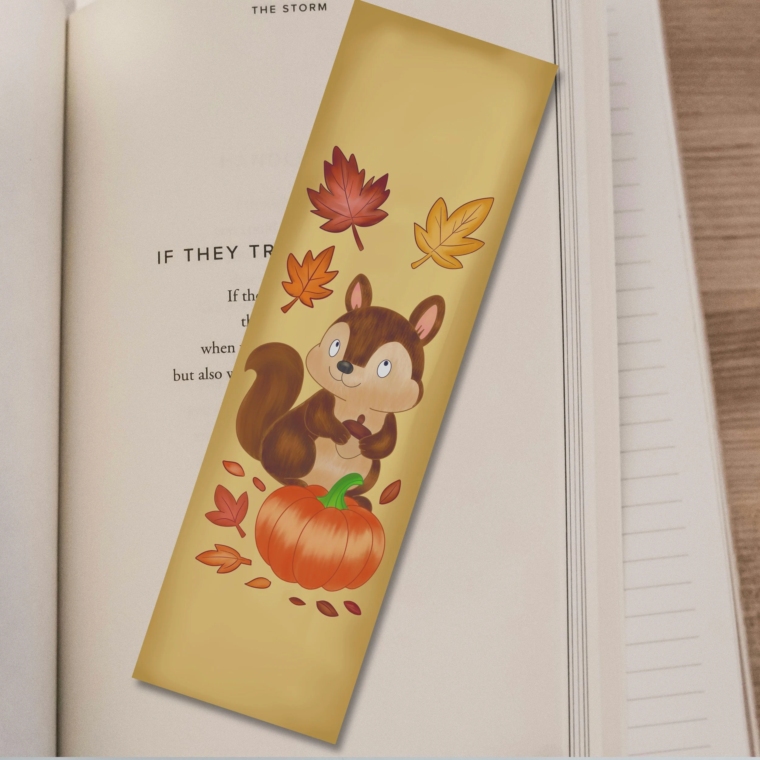 A fall-themed bookmark with a cartoon squirrel holding an acorn, surrounded by autumn leaves and a pumpkin, placed on an open book.