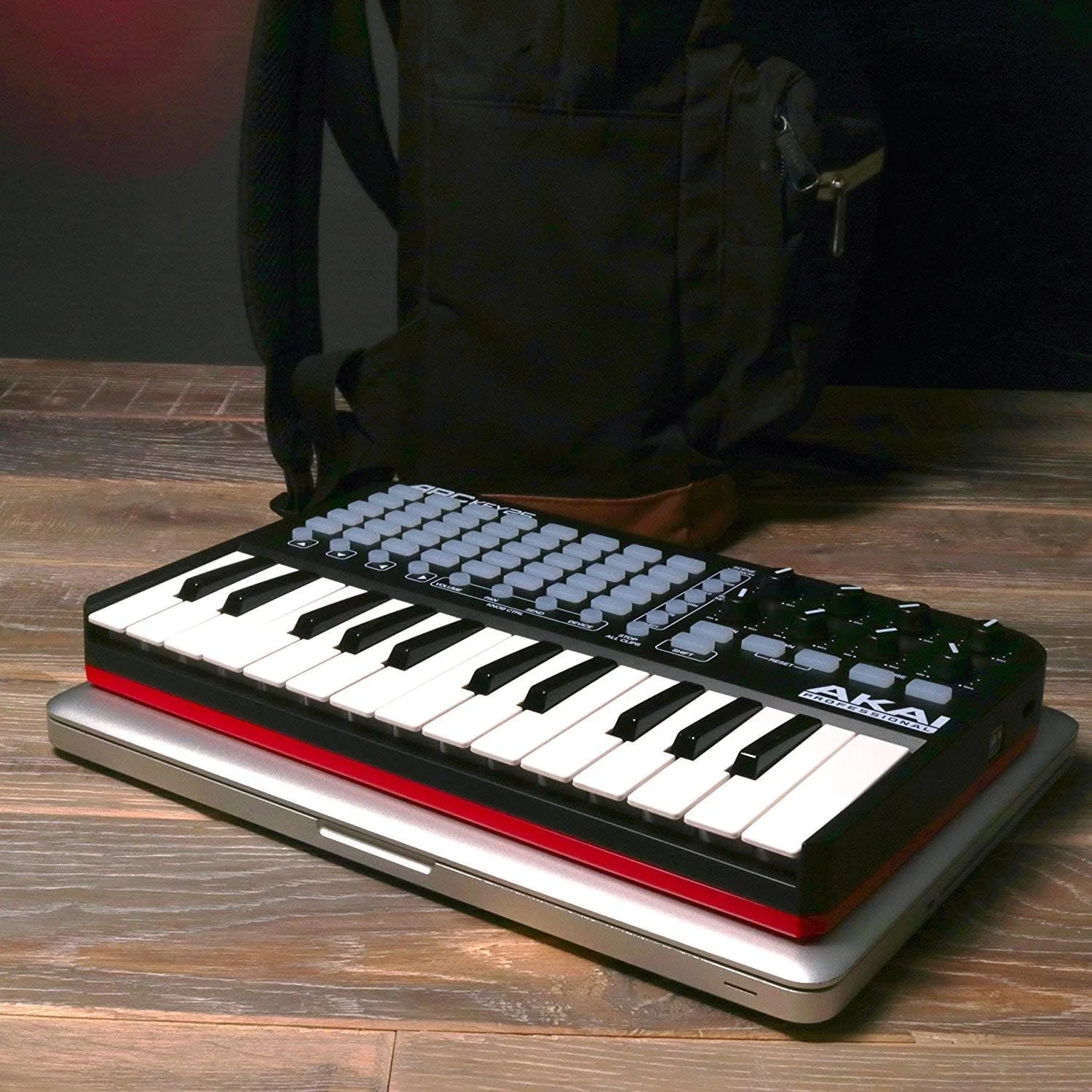 A compact electronic keyboard placed on top of a closed laptop, with a black backpack in the background on a wooden floor.