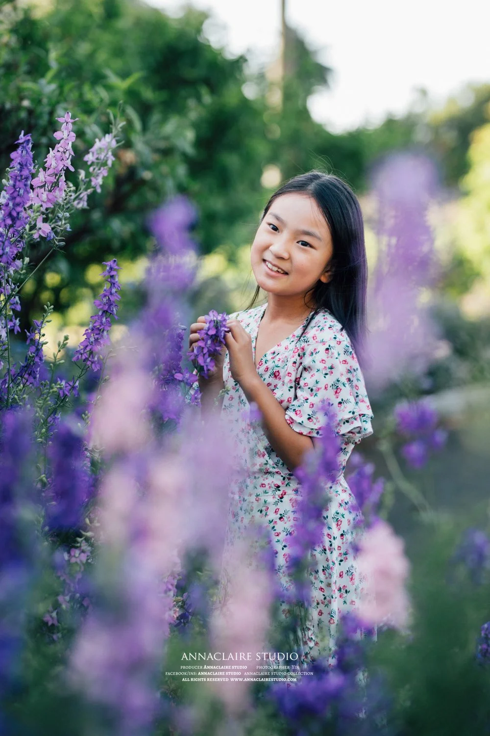 A young girl in a floral dress standing amongst purple flowers, smiling, at parramatta park 