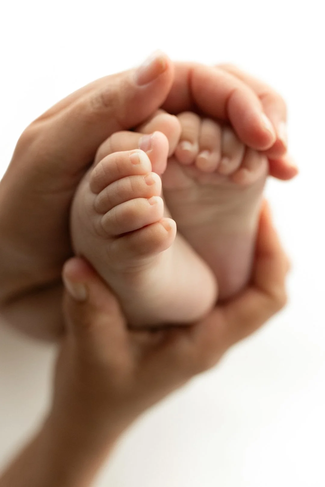 A close-up photo of an adult's hand holding a baby's hand, with the baby's tiny fingers curled around the adult's finger.