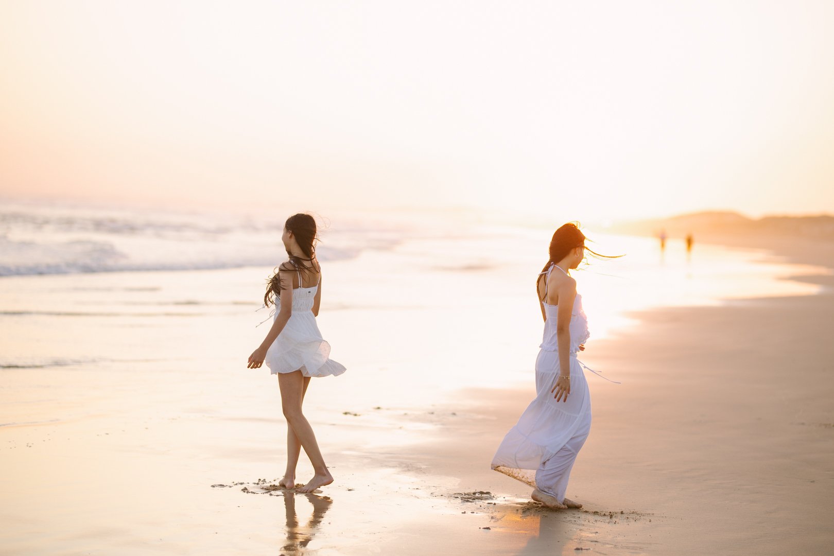 Anna and Clarie walking along the Anna bay beach at sunset, wearing white dresses 