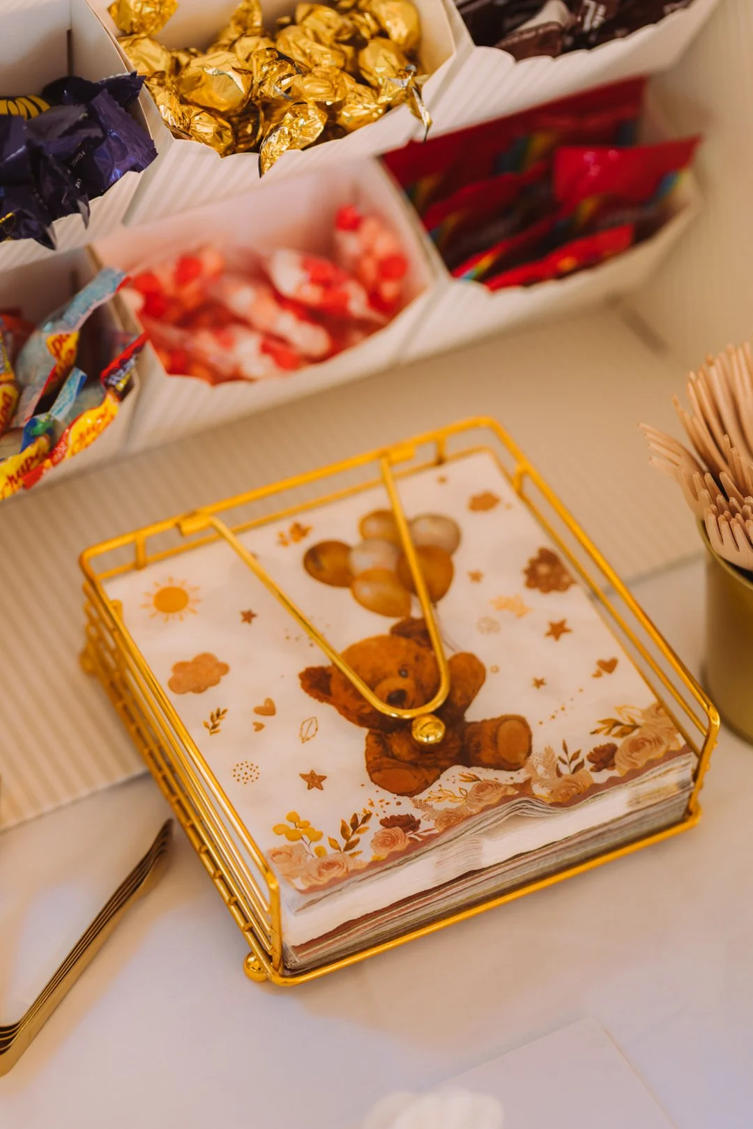 A decorative tissue box featuring a teddy bear illustration, placed on a table with various candies in the background.