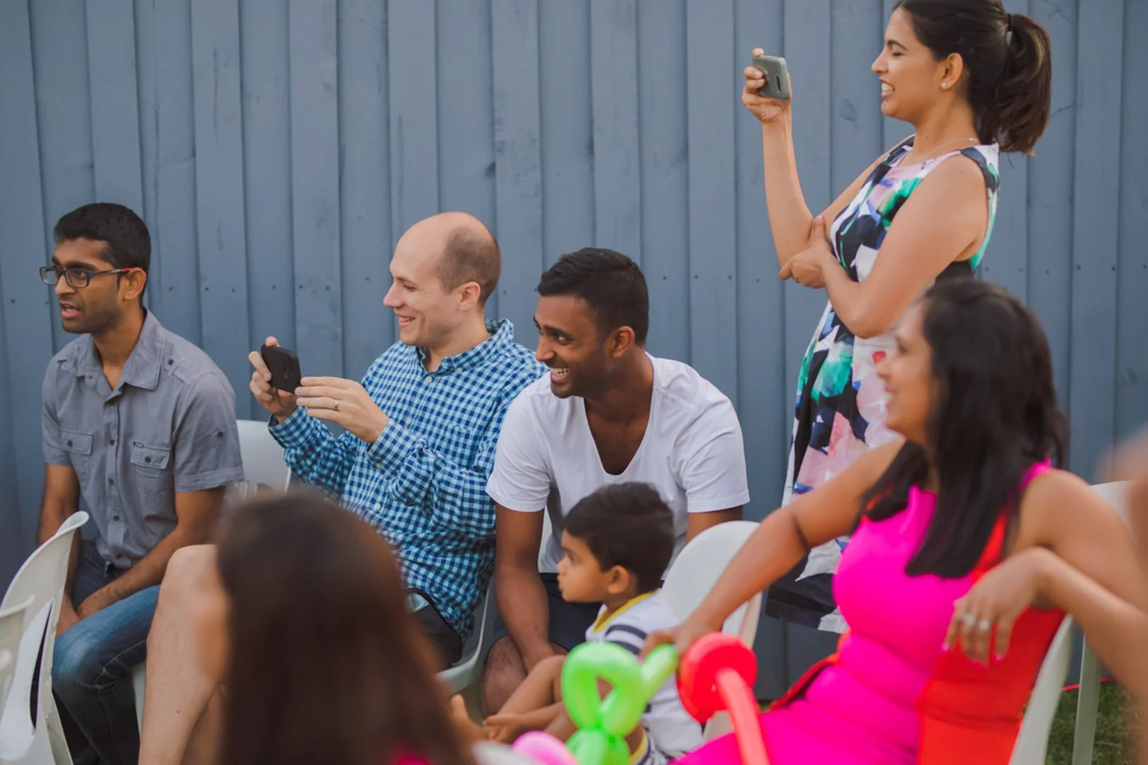 People gathered at an outdoor event, some taking photos and videos with their phones, smiling and enjoying the moment.
