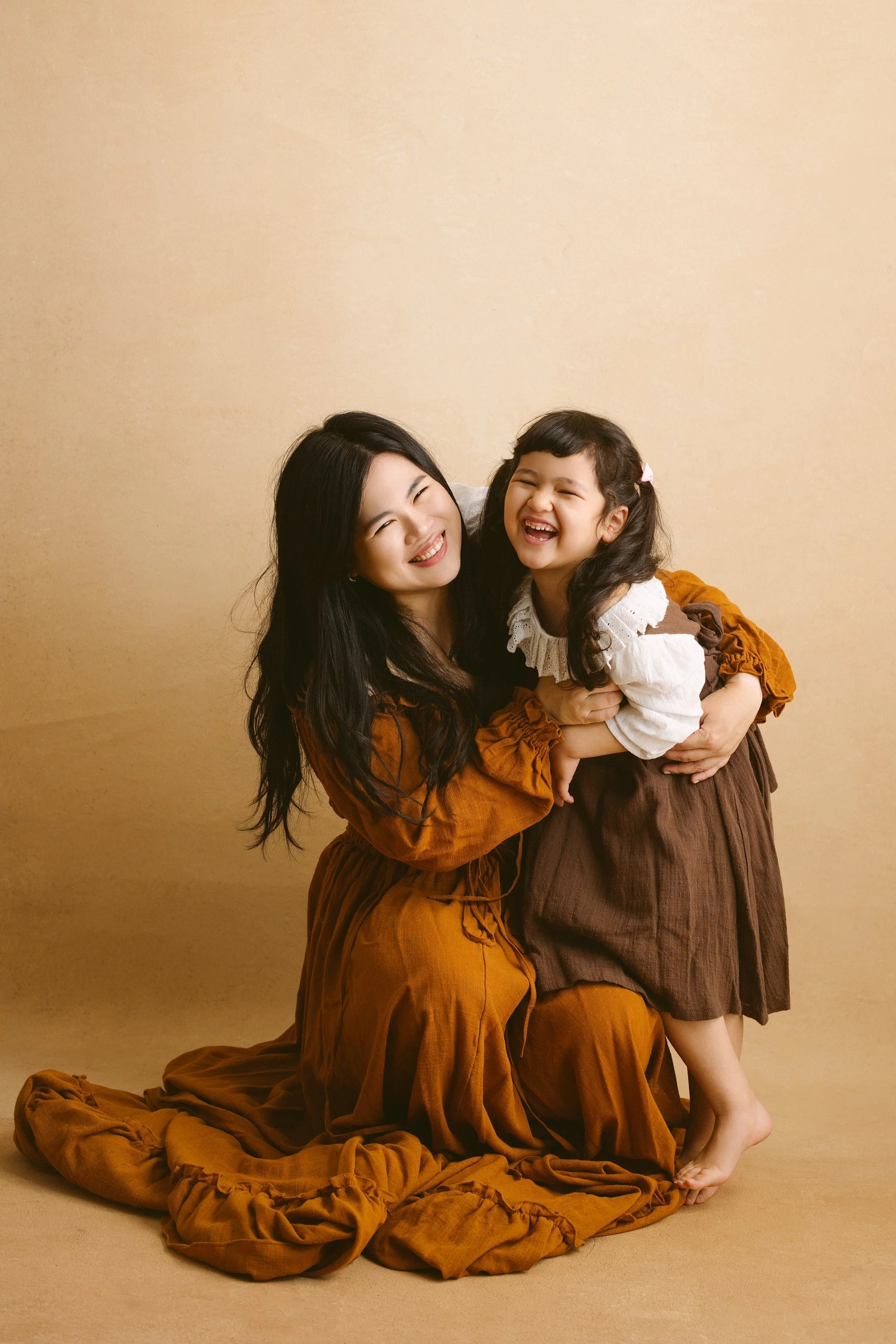 A woman and young girl sharing a joyful moment, with the woman kneeling and the girl standing on her bare foot, both smiling.