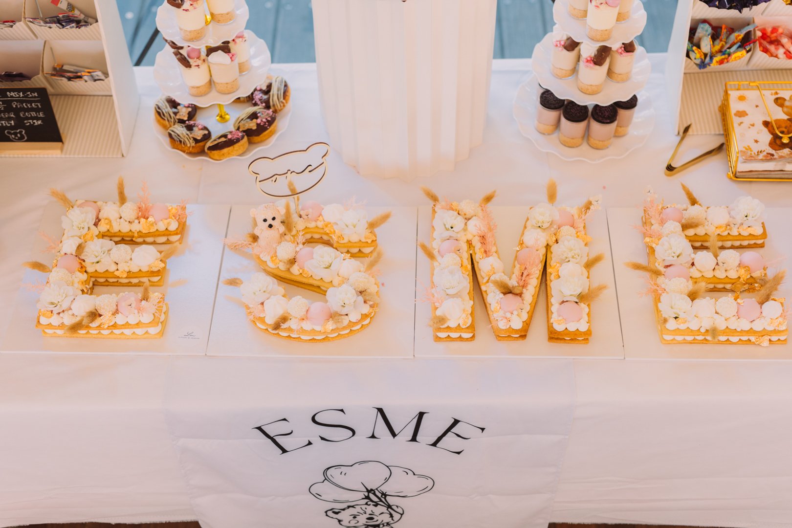 Decorative table display featuring large floral letter cookies spelling 'ESME' with bunny-themed decorations, and a tray of small desserts with panda faces and macarons.