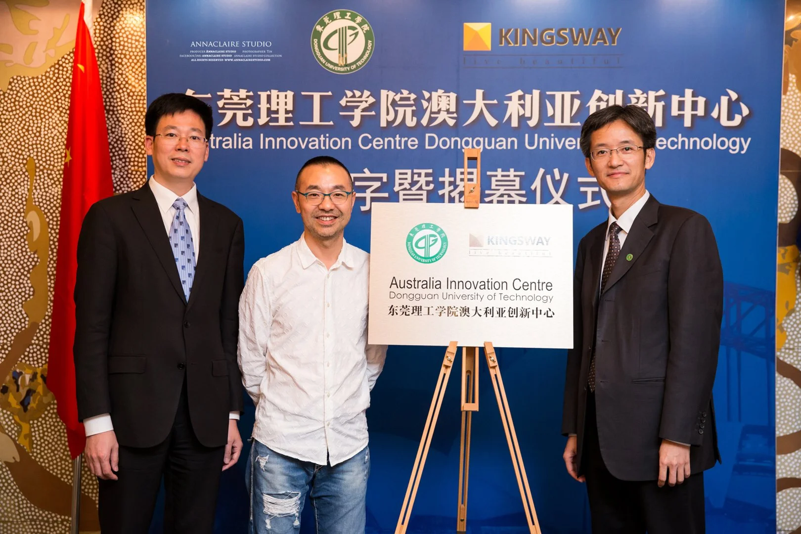Three men standing in front of a blue backdrop at a ceremony, with a sign on an easel that reads, "Australia Innovation Centre Dongguan University of Technology" in English and Chinese, and logos of the university and Kingsway.