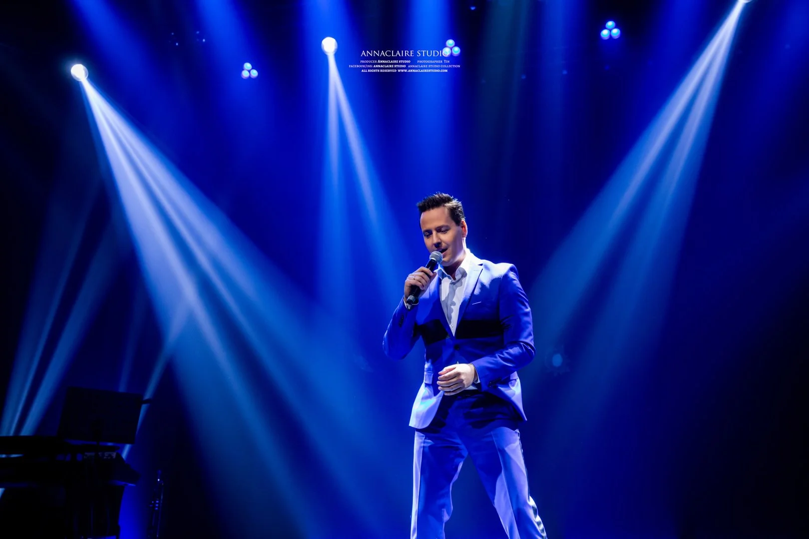 Singer in a blue suit performing on stage under blue and white spotlights.
