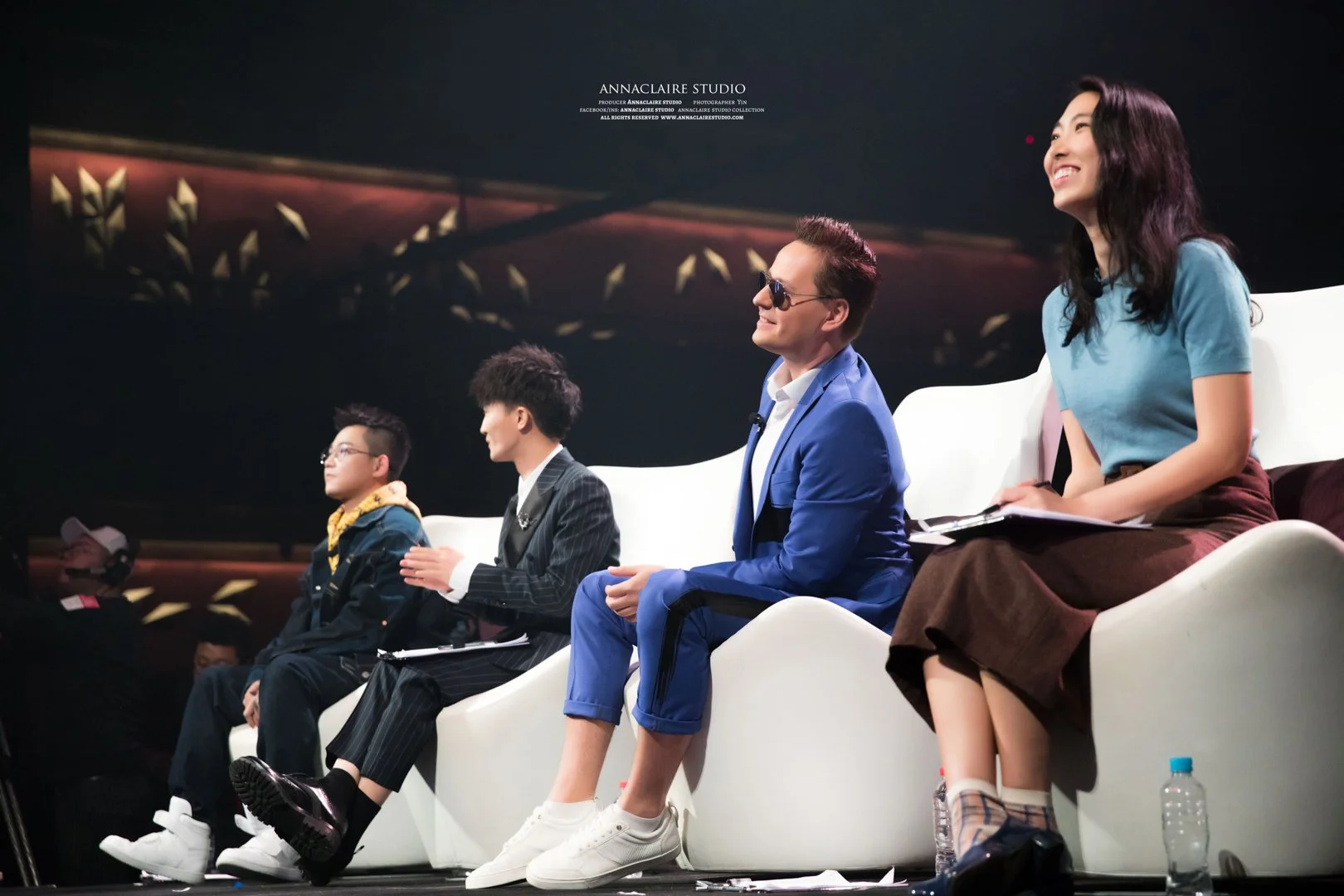 Four people sitting on a stage, participating in a panel or discussion, with a dark background and the text 'Annaclaire Studio' at the top.