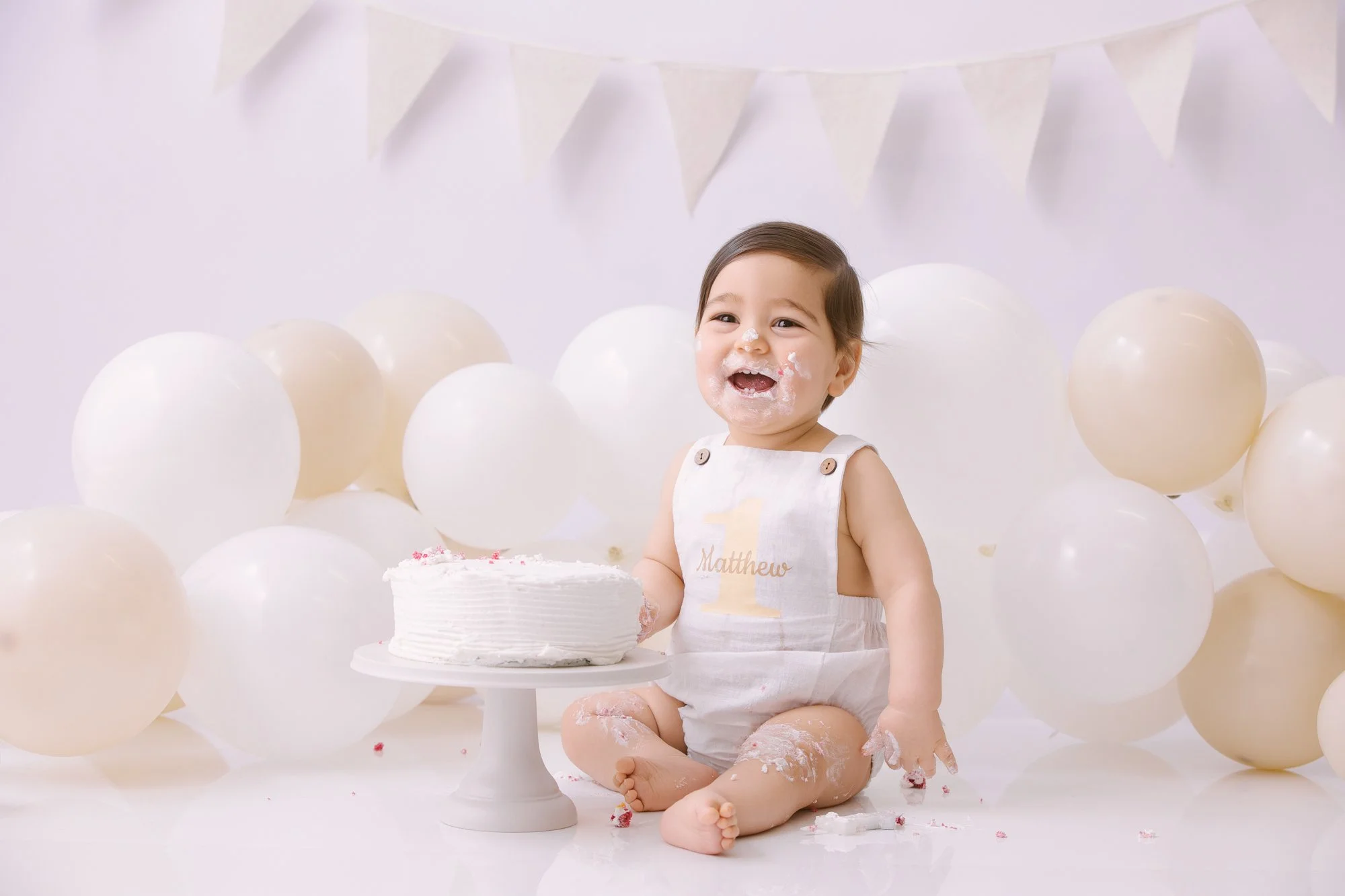 Happy baby boy with cake and balloons at birthday celebration.