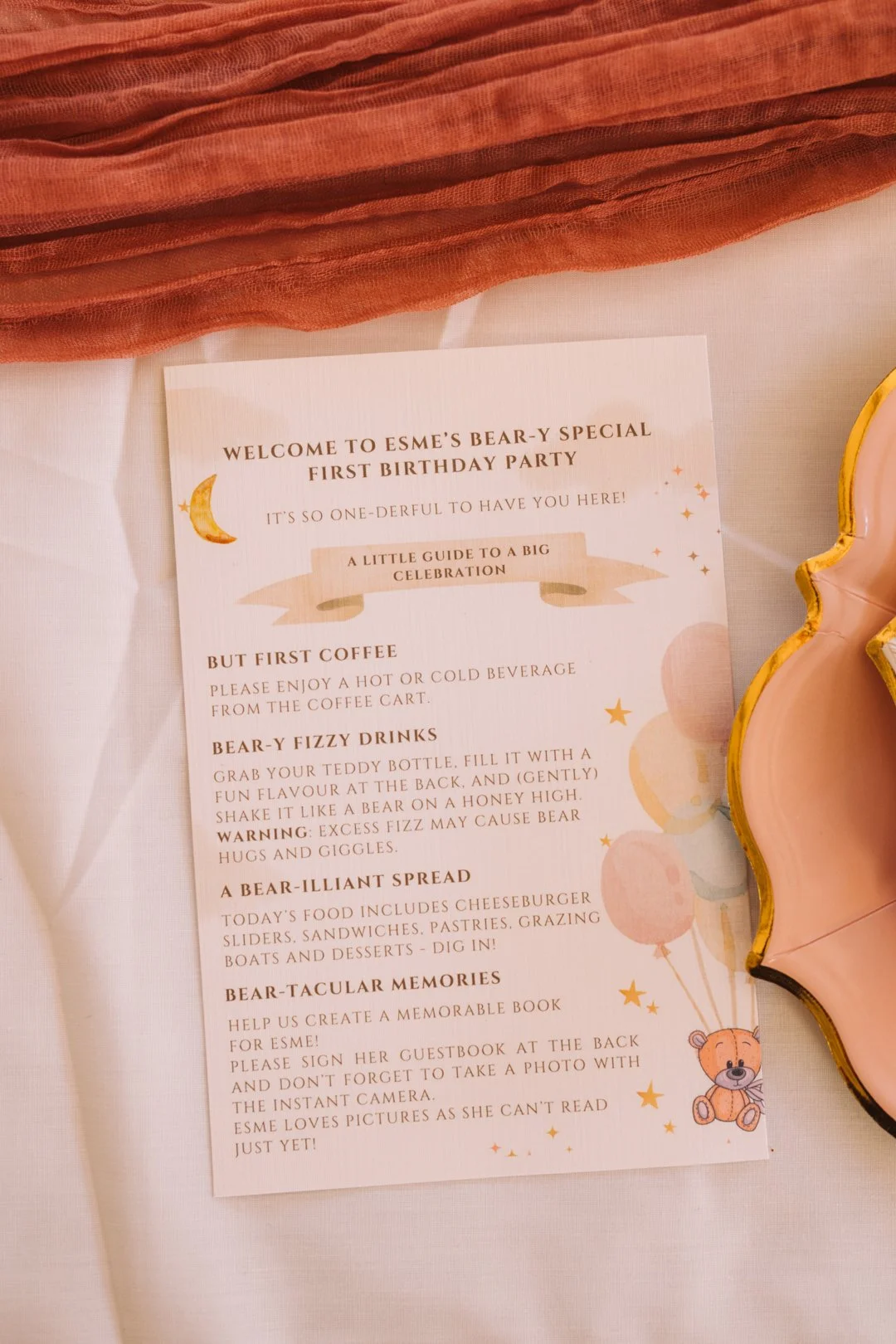 Invitation card for Esme's first birthday party with a teddy bear illustration, listing activities like drinks, snacks, and a photo booth.