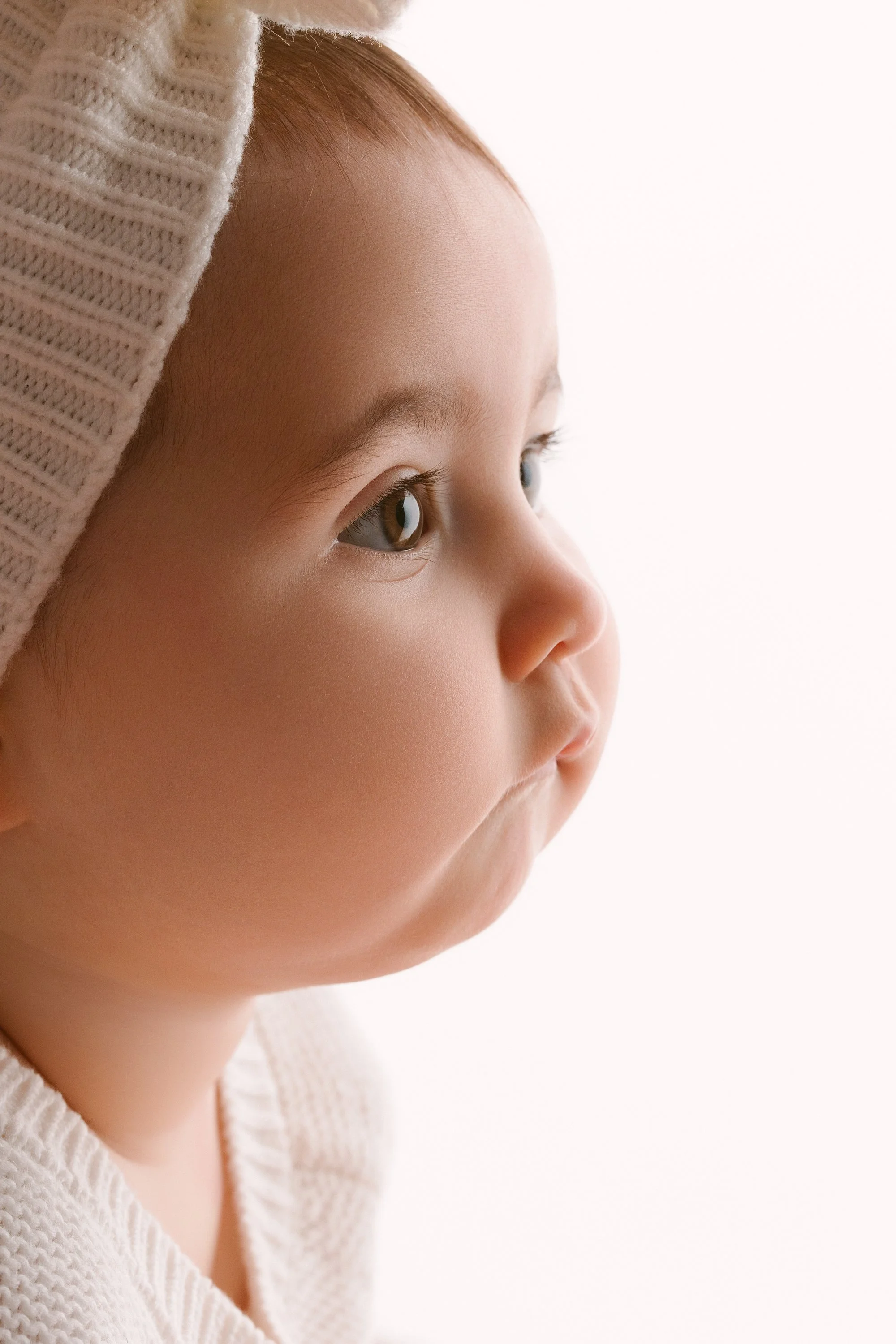 Close-up profile of a young child with light skin, brown hair, and hazel eyes, wearing a knit hat and sweater.