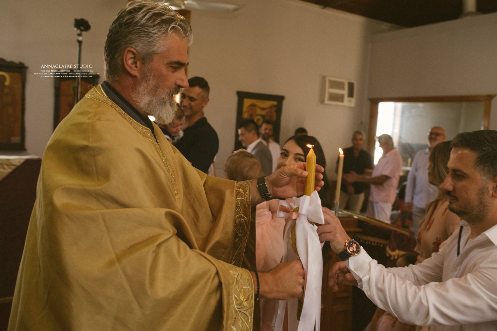 Man in gold ceremonial robe lighting a candle at a religious ceremony, surrounded by people including a woman with a child, in a church or religious setting.