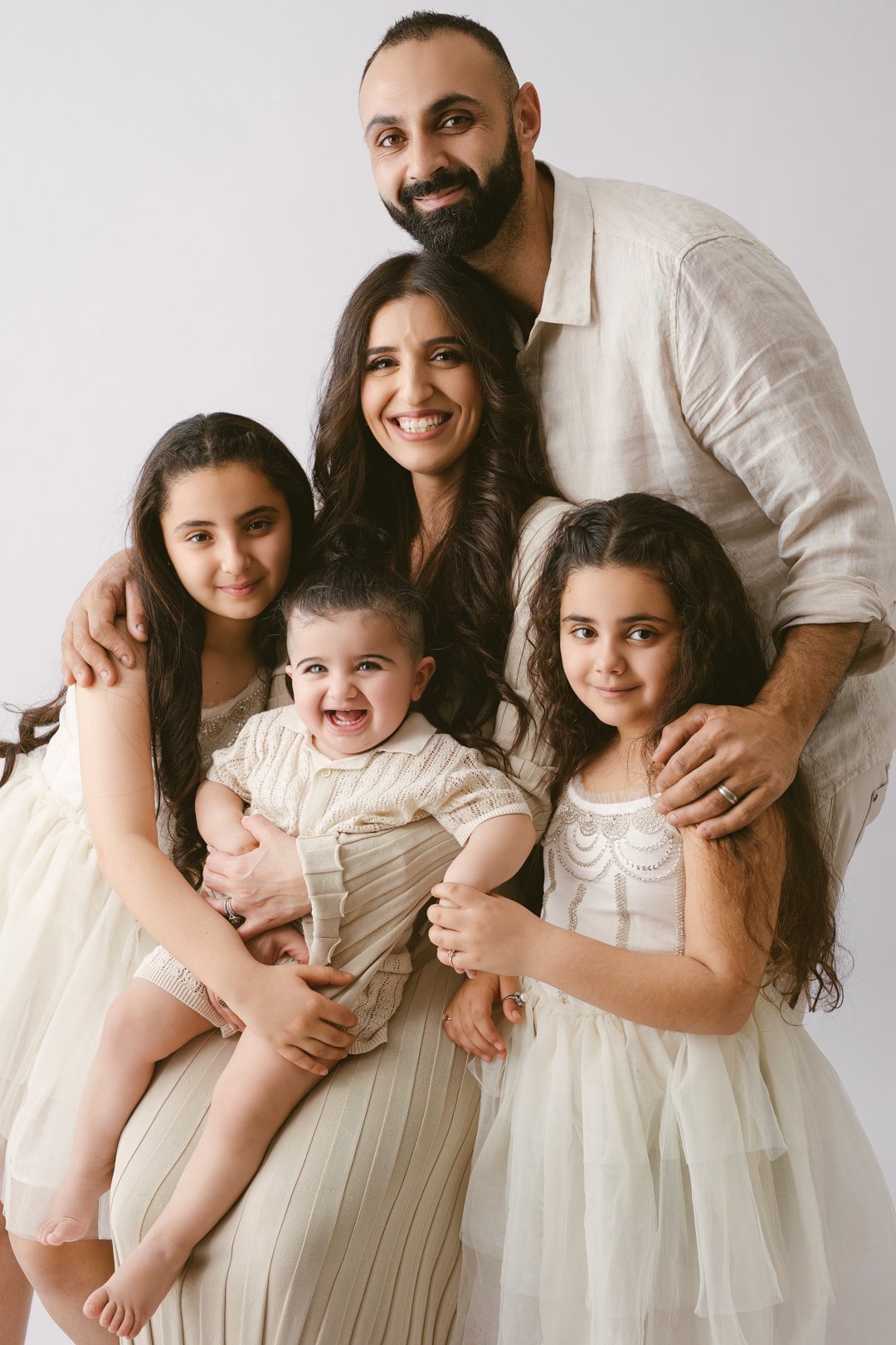 A happy family of six, including a father, mother, and four daughters, poses together against a plain white background.