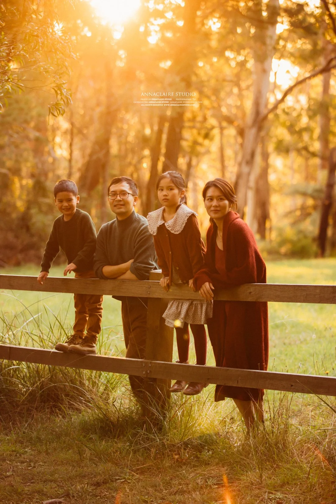 Family of four, including two children, standing on a wooden fence in a forest during golden hour, surrounded by trees with fall foliage at Mt Wilson.