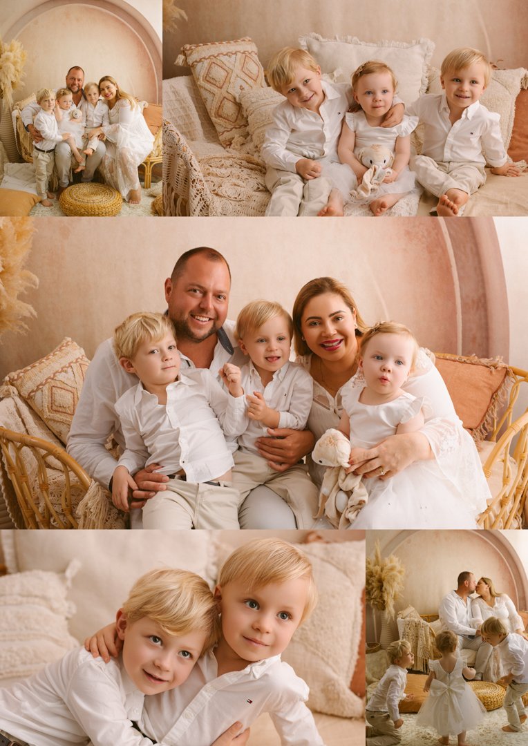 A family of five with three young children, two boys and a girl, all dressed in white, sitting and standing on a vintage-style sofa in a cozy, warmly lit room with soft pastel decor. The family is smiling and interacting, capturing a joyful moment.